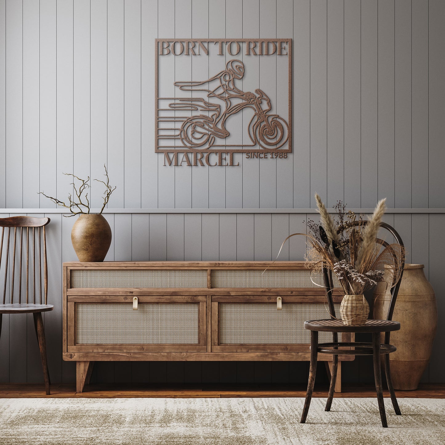 A rustic living room features a wooden sideboard, a chair, and a vase with dried plants. Completing the scene is the "Biking Metal Line Art," showcasing a wall-mounted metal sign of a motorcyclist with the text "Born to Ride" and "Marcel Since 1988," adding an edgy touch to this inviting home decor.