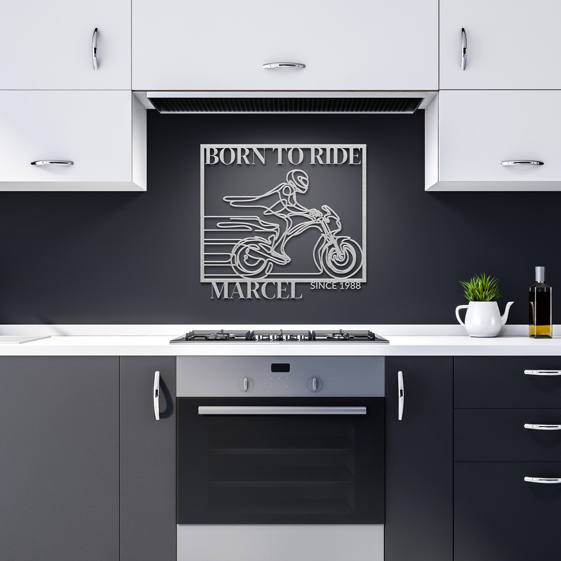A modern kitchen featuring white cabinets and a black backsplash is enhanced by the Biking Metal Line Art, a motorcycle-themed metal sign crafted from 18 gauge steel that reads "Born to Ride Marcel Since 1988" above the stove. This distinctive piece infuses an adventurous spirit into your home decor.