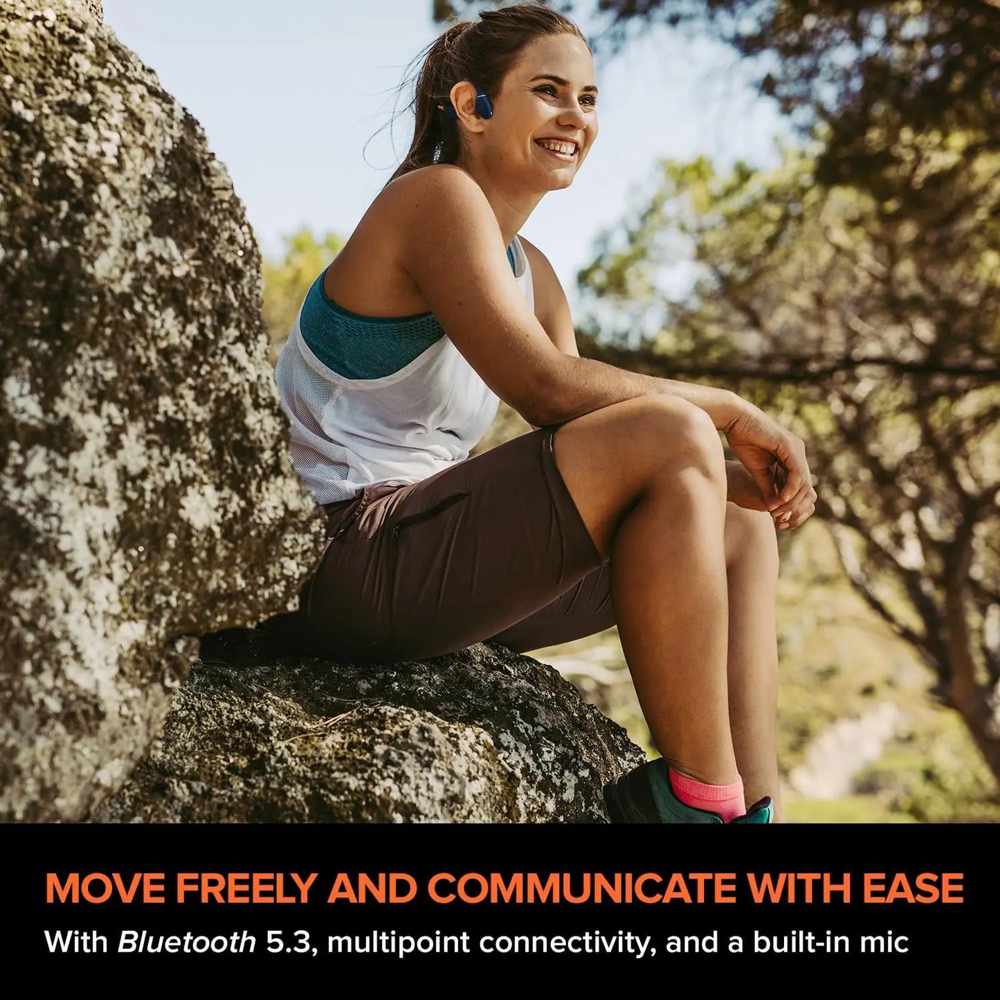 A woman with Bluetooth earphones sits on a rock, smiling amidst the trees. Text highlights Bluetooth 5.3, multipoint connectivity, bone conduction tech, and built-in mic in the Creative Outlier Free Pro+ Wireless Waterproof Headphones with Adjustable Transducers and 8 GB MP3 Mic.
