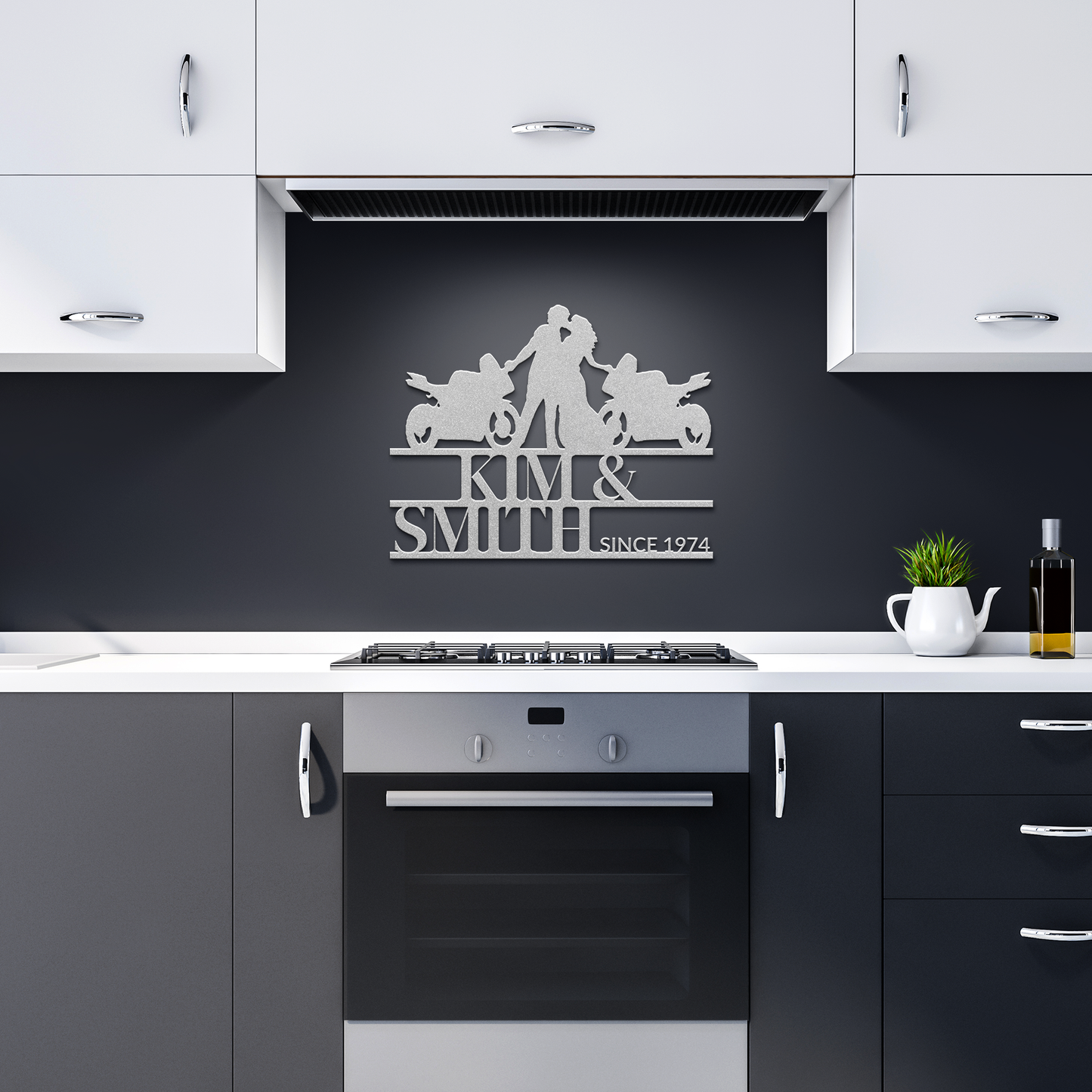 Modern kitchen with white cabinets, a black backsplash featuring a Custom Motorcycle Couple Metallic Wall Art Laser Cut Metal Sign personalized with the "Kim & Smith Since 1974" logo, and a sleek black countertop adorned with a potted plant and an oil bottle.