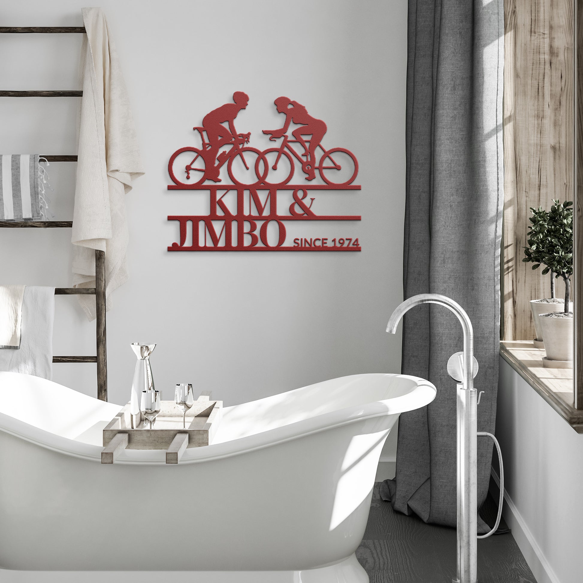 Bathroom featuring a freestanding tub and ladder shelf, highlighted by the Custom Cyclist Couple Metal Wall Art Sign. This unique decor showcases two cyclists with the personalized text "Kim & Jimbo Since 1974." Natural light streams in through a window adorned with gray curtains, making it an ideal home decor gift for cycling enthusiasts.