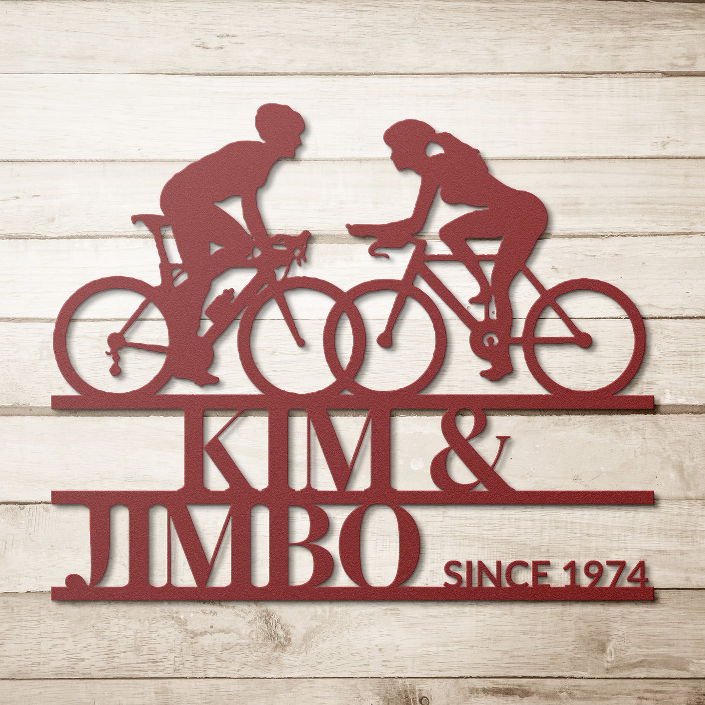 Custom Cyclist Couple Metal Wall Art Sign featuring a metal silhouette of two cyclists with the text "Kim & Jimbo Since 1974" on a wooden backdrop, making it an ideal personalized home decor gift.