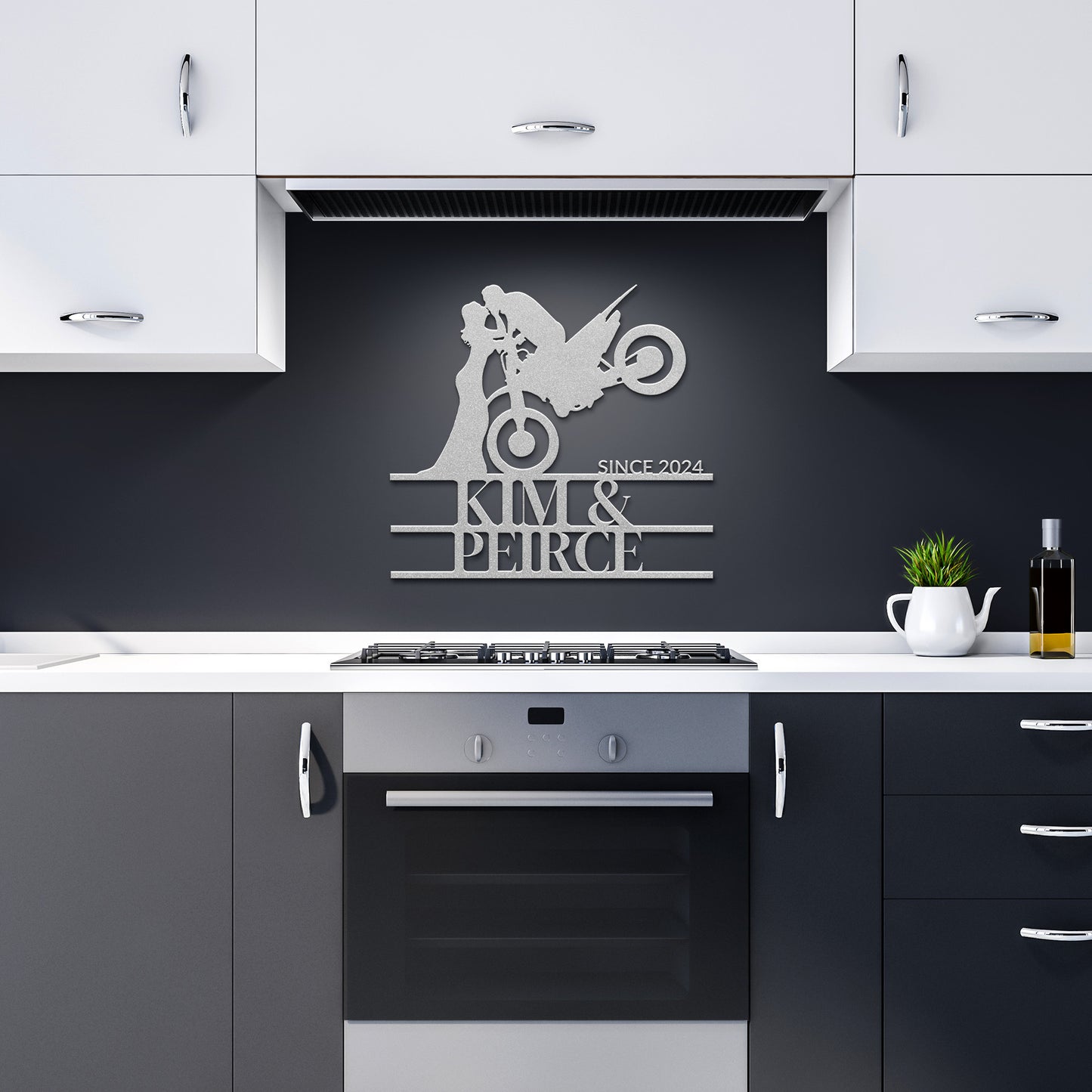 In the modern kitchen, the stylish decor is enhanced by a sleek piece of wall art: the "Custom Motorcycle Couple Metal Wall Art," featuring a couple on a motorcycle with "Kim & Peirce Since 2024" meticulously etched into 18-gauge steel. Against the black backsplash, this metal sign stands out beautifully amidst white cabinets and black countertops.