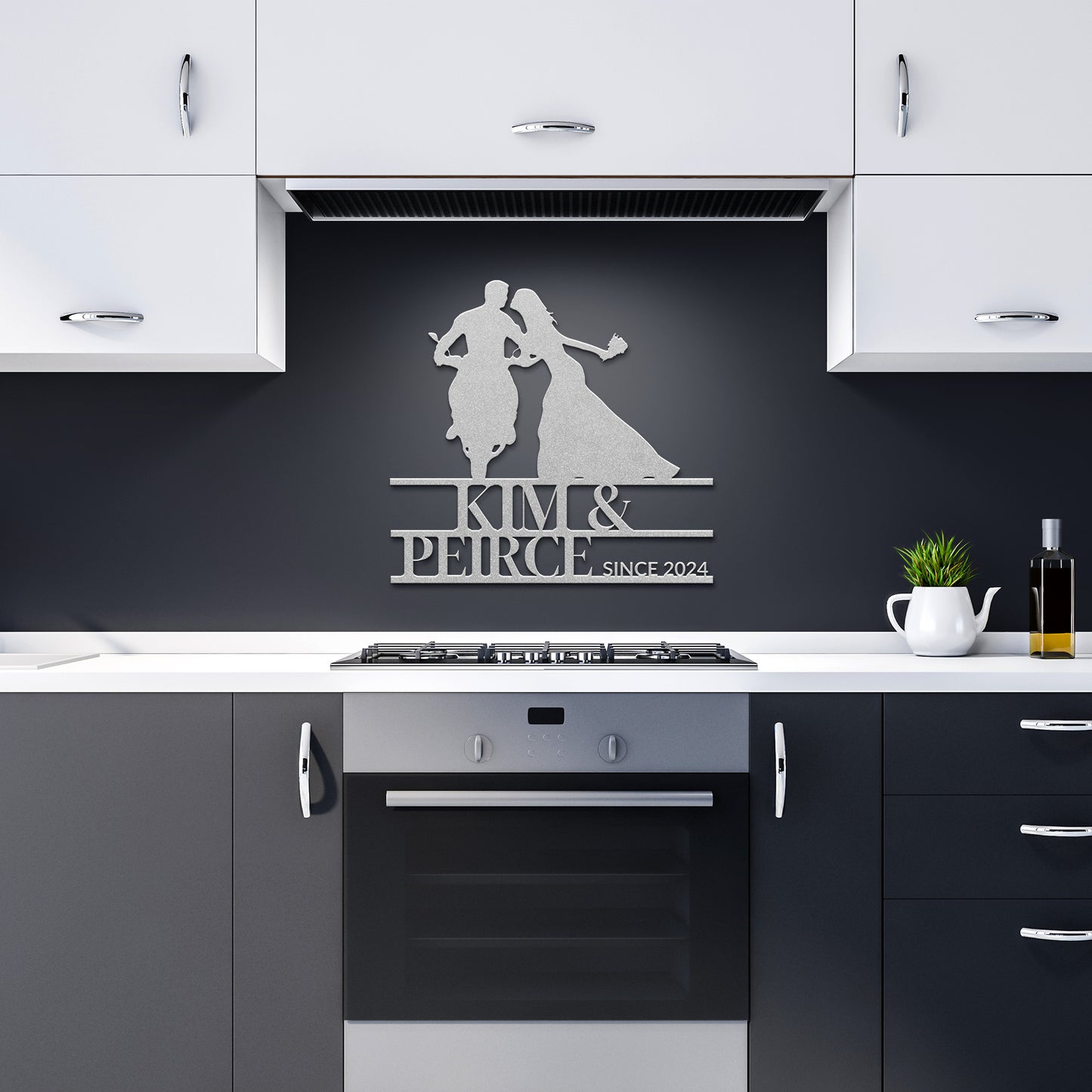 A modern kitchen with white upper cabinets and dark lower cabinets showcases a sleek 18-gauge steel piece that reads "Kim & Peirce Since 2024," featuring silhouettes of two dancers. This Custom Motorcycle Couple Metal Wall Art adds a unique touch to the home decor above the stove.