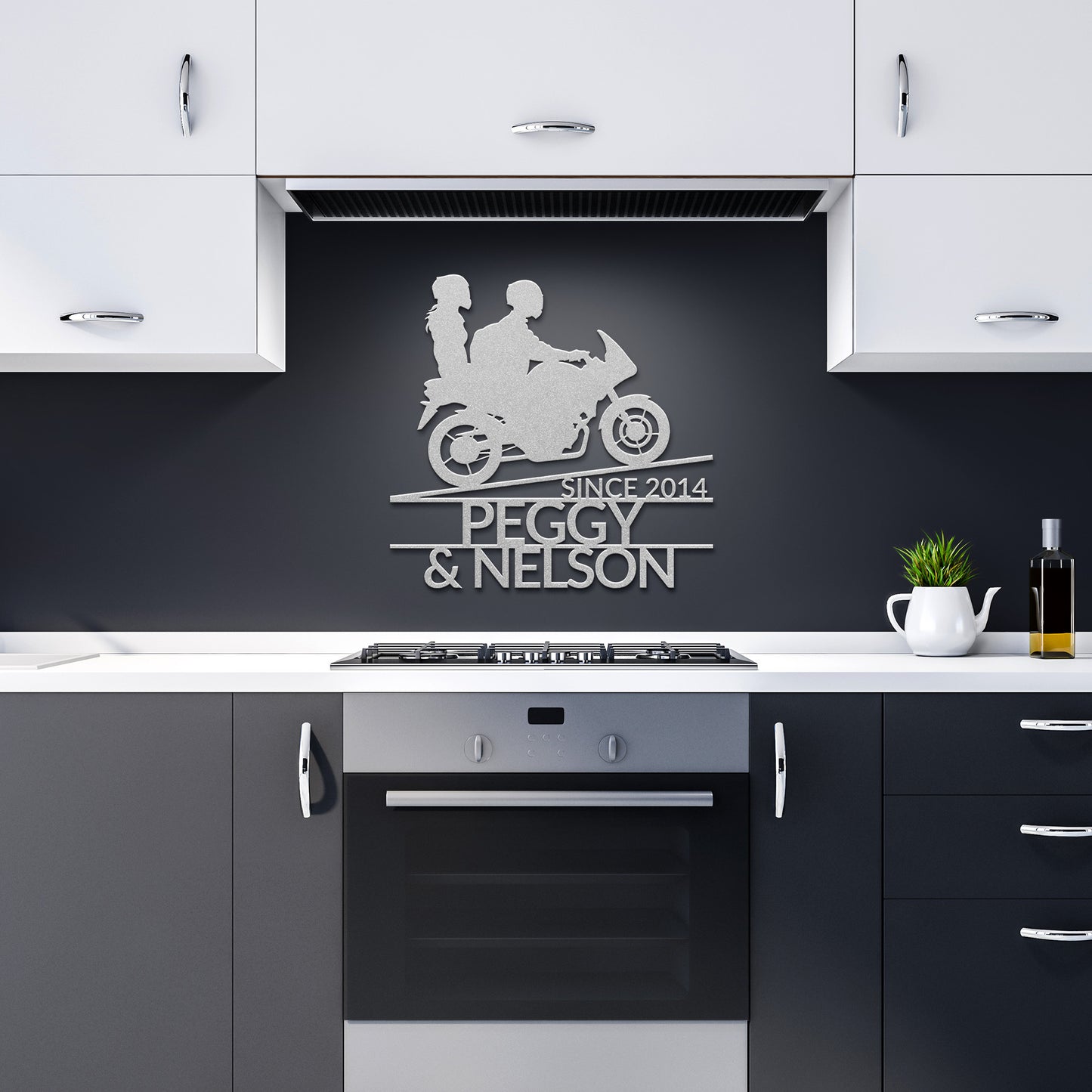 The modern kitchen features black and white cabinets, with a sleek **Custom Motorcycle Couple Metallic Wall Art** on the wall displaying a silver motorcycle silhouette and the words "Since 2014 Peggy & Nelson." A potted plant and oil bottle add flair to the home decor.