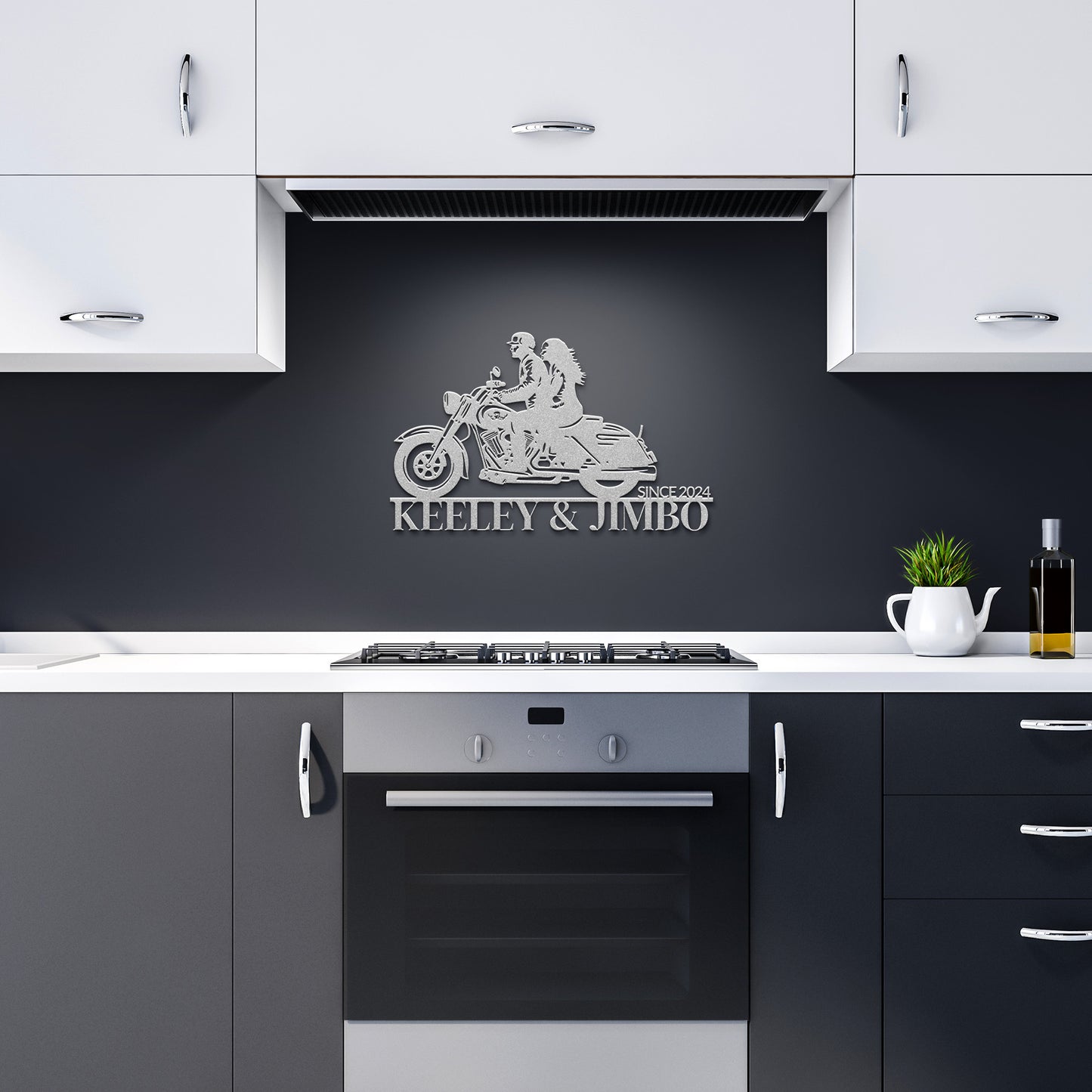 A modern kitchen with white cabinets and black countertops features a striking Custom Motorcycle Couple Metallic Wall Art. Crafted from 18-gauge steel, it showcases a motorcycle and "KEELEY & JIMBO SINCE 2024," adding unique flair to the decor above the stove on the black wall.