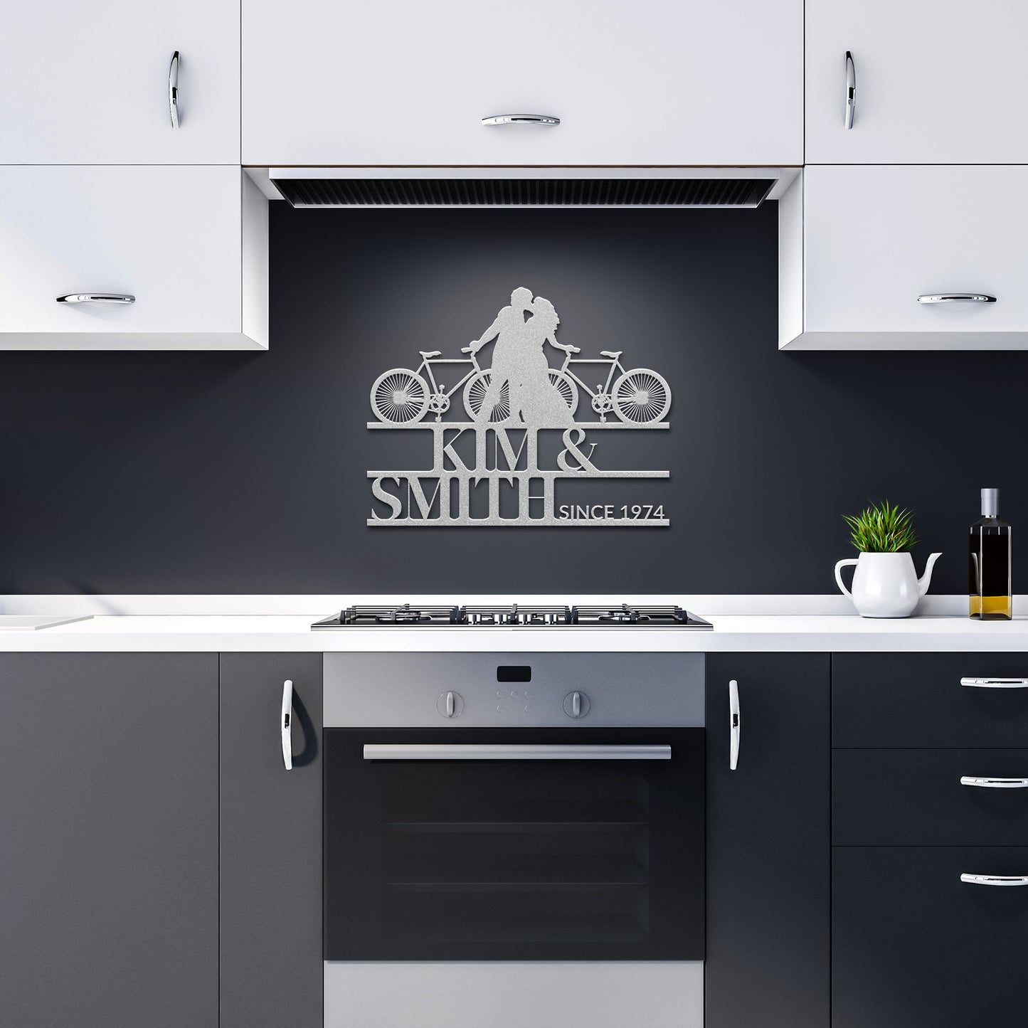 A modern kitchen in gray and white is enhanced by the elegant Cycling Couple Metal Sign, featuring a couple with a bicycle and "Kim & Smith Since 1974" text. Crafted from 18 gauge steel, it adds unique charm above the oven.