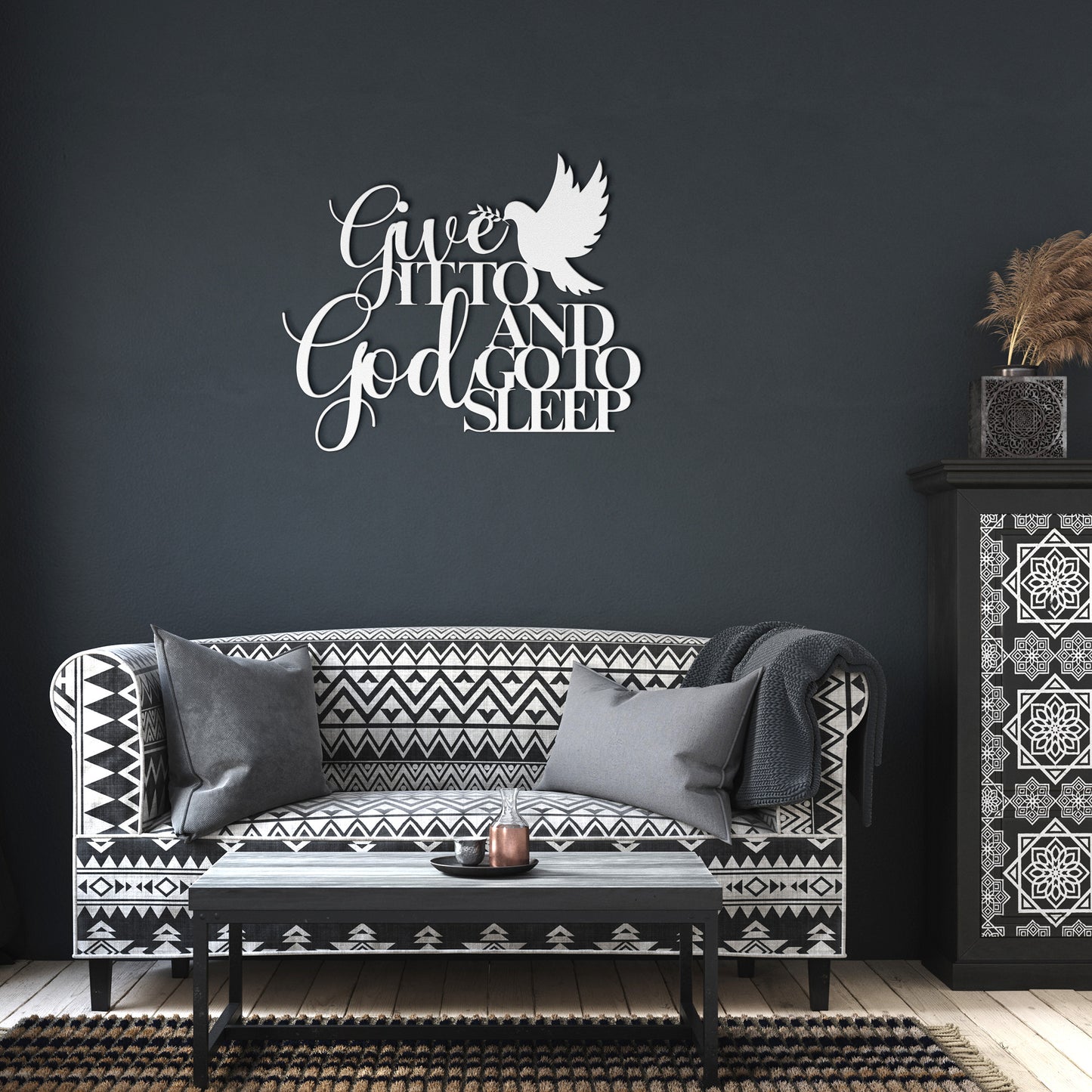A modern living room featuring a black and white patterned sofa, grey pillows, a black coffee table, and the "Give It To God And Go To Sleep" Christian Metal Sign with a white dove graphic—an inspiring quote that truly enhances the space.