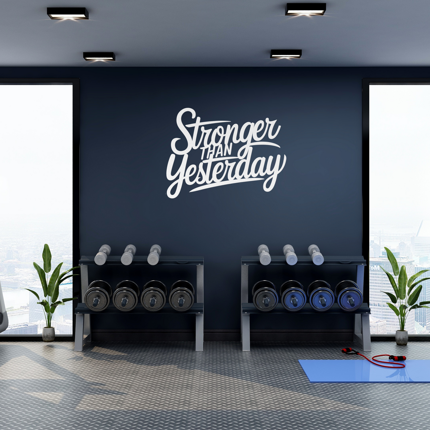 A modern gym with large windows offers a city view and sleek decor. Lush plants flank two sets of dumbbells on racks. A royal blue wall displays the "Stronger Than Yesterday Metal Sign." Completing the space are a blue exercise mat and resistance bands.