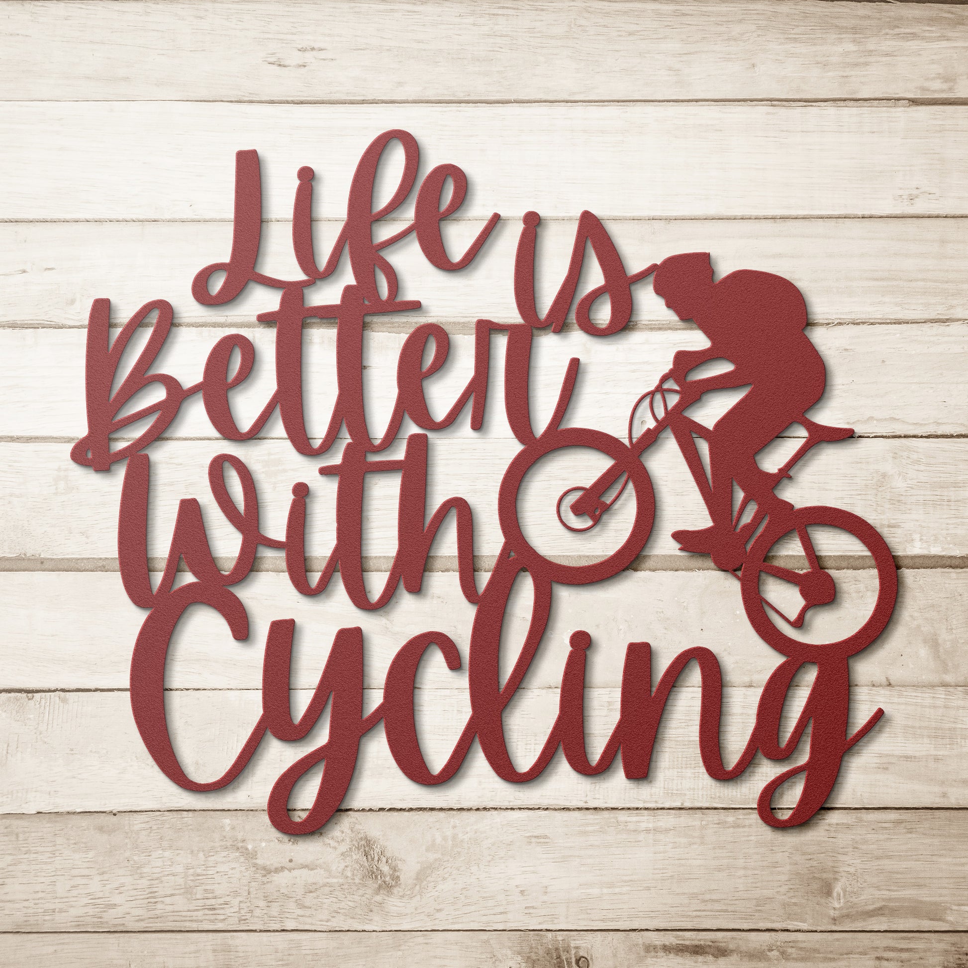 A brick wall with a wooden door, a durable Life Is Better With Cycling Metal Art sign, an exterior light, and a small potted plant with white flowers.