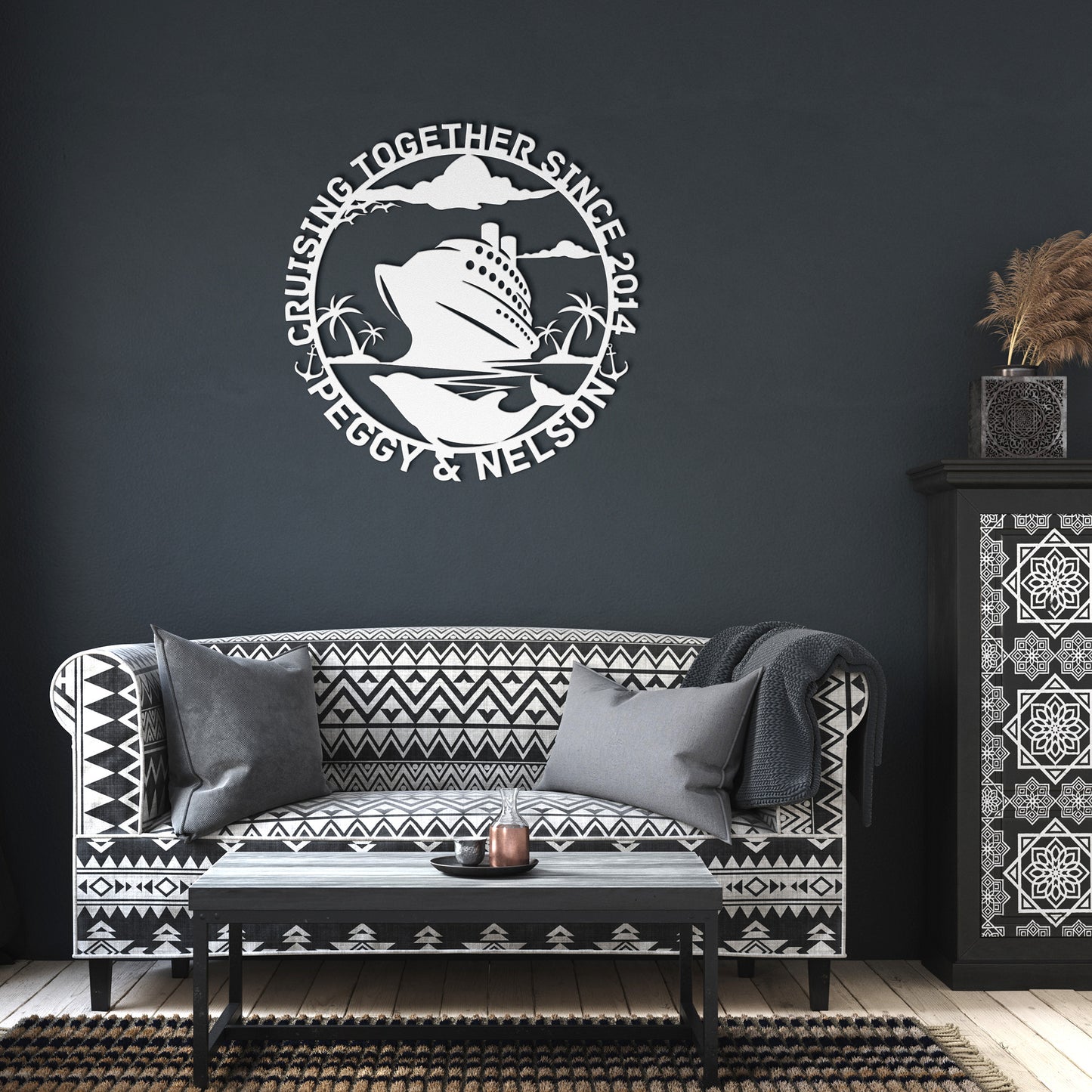 In the living room, a patterned sofa is adorned with cushions and a blanket. Above it hangs the Personalized Cruise Couples Metal Wall Art crafted from 18 gauge steel. It reads "Cruising Together Since 2014, Peggy & Nelson," featuring a cruise ship and palm trees, adding charm to the home decor.