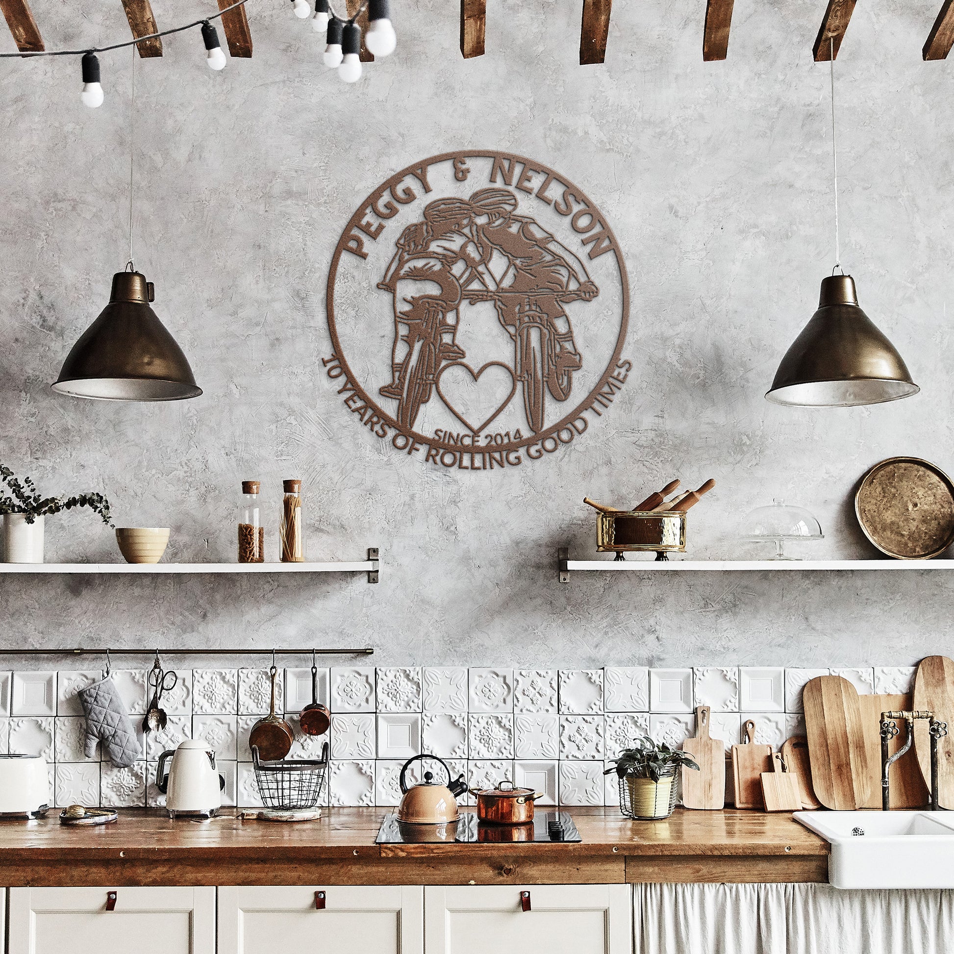In a rustic kitchen, a Personalized Cycling Couple on Mountain Bikes Metal Art sign adorns the concrete wall above shelves and a white tile backsplash. It displays bicycles and the text, "Peggy & Nelson, 50 years of rolling good times since 2014.
