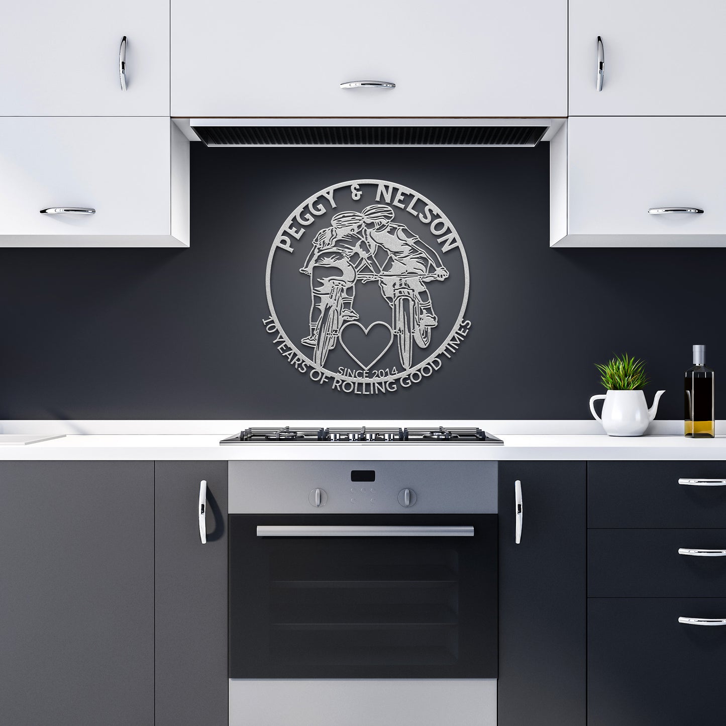 A kitchen with black and white cabinets showcases a wall decoration depicting two motorcyclists, featuring the text "Peggy & Nelson: 40 Years of Rolling Good Times," and a heart above an oven—an ideal version of the Personalized Cycling Couple on Mountain Bikes Metal Art for those who cherish their journey together.