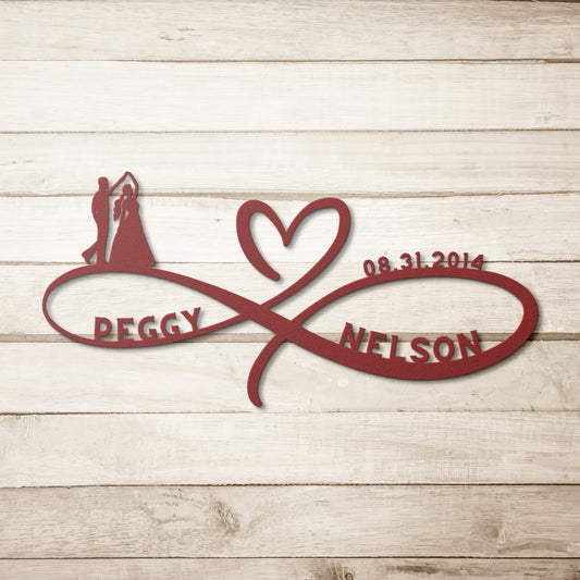 A wooden door with a decorative glass panel is set in a brick wall. A Personalized Infinity Love Heart Metal Sign For Wedding Couples reading “Peggy ♡ Nelson” and a lantern are mounted on the wall. A potted plant with white flowers sits near the door, adding a charming touch to the home decor.