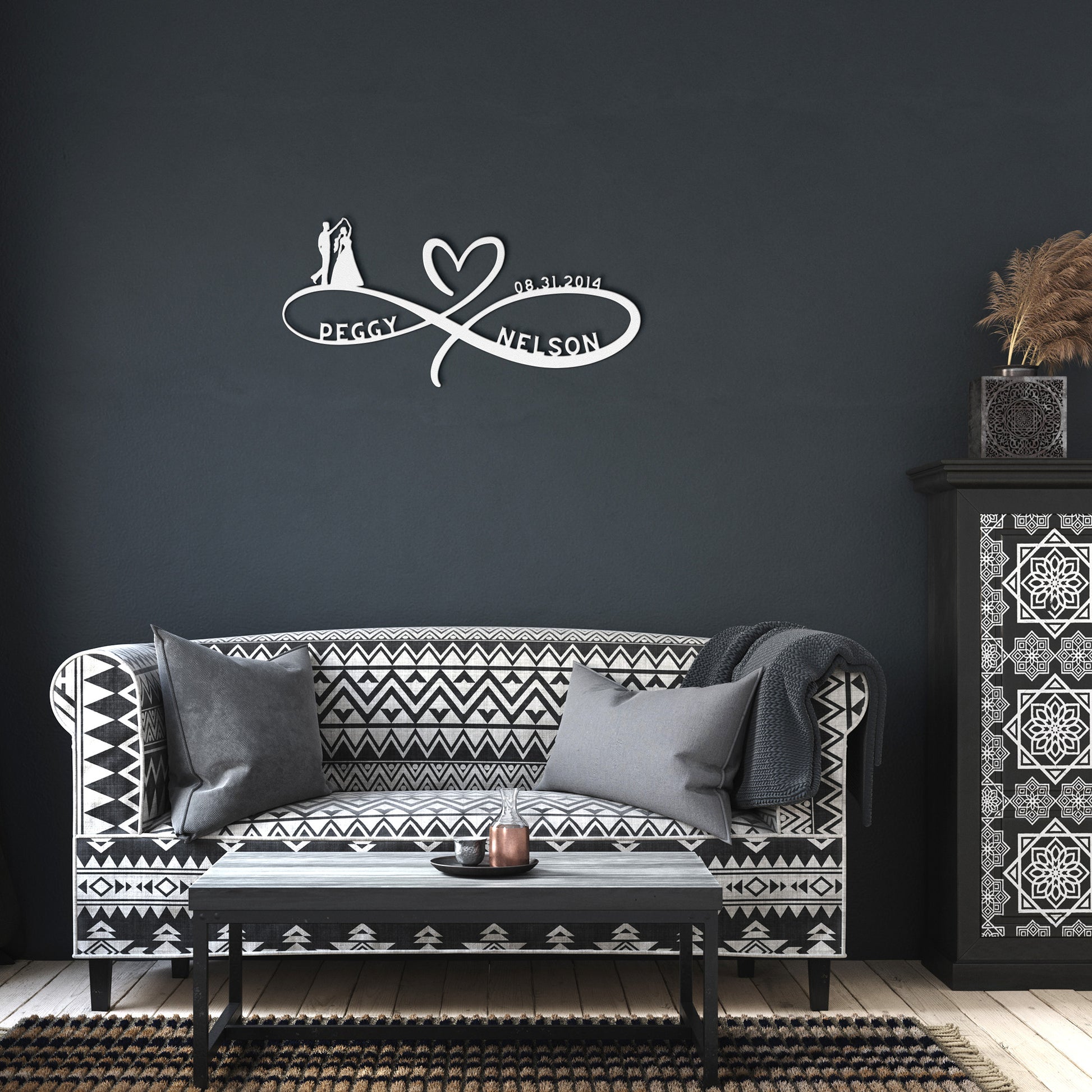 A wooden door with a decorative glass panel is set in a brick wall. A Personalized Infinity Love Heart Metal Sign For Wedding Couples reading “Peggy ♡ Nelson” and a lantern are mounted on the wall. A potted plant with white flowers sits near the door, adding a charming touch to the home decor.