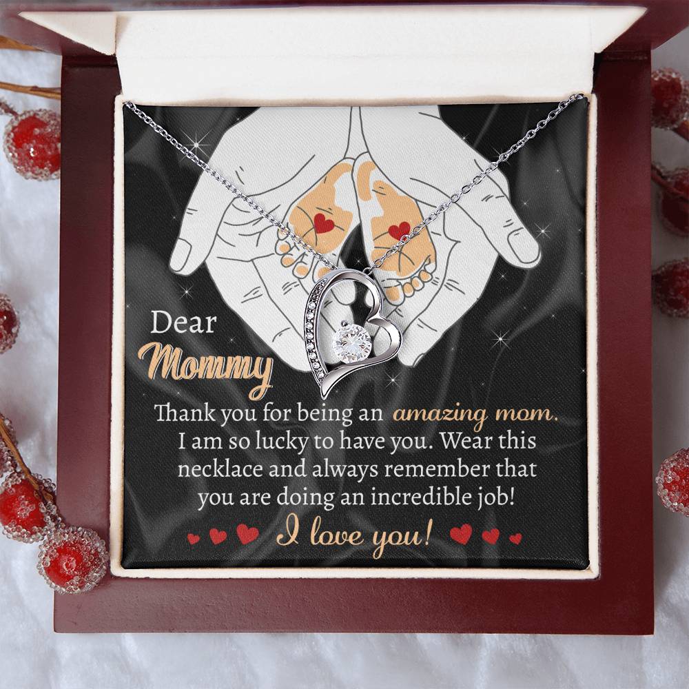 A personalized gift, the "To Mom To Be, An Incredible Job - Forever Love Necklace," is displayed in a box with a message to "Mommy," thanking her for being amazing and expressing love. The box features an illustration of hands holding a heart, embellished with intricate heart details.