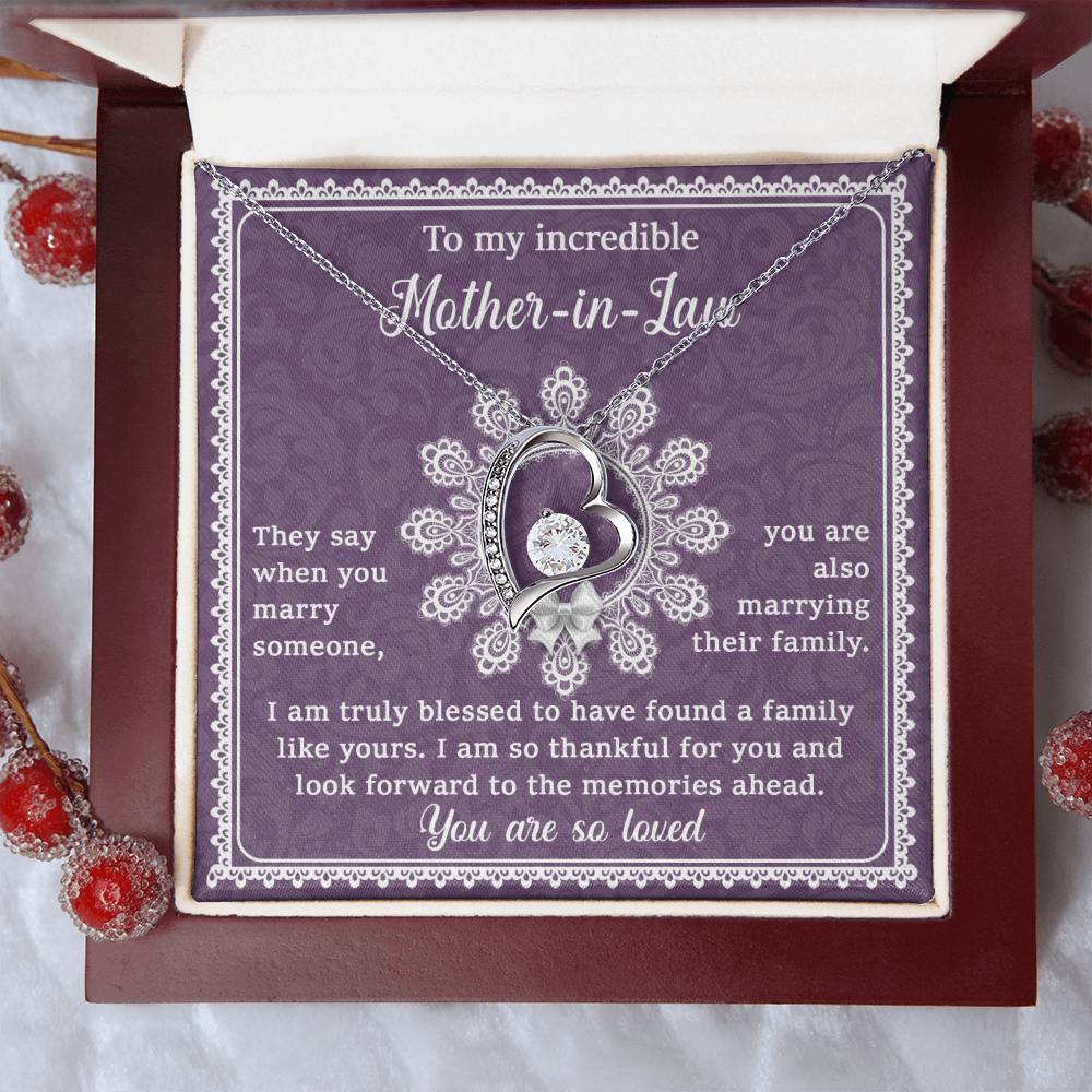 A 14k white gold finish, heart-shaped To Mother-In-Law, Family Like Yours - Forever Love Necklace on a purple card with a heartfelt message to a mother-in-law inside a red jewelry box. Frosted red berries are arranged around the box, making it the perfect unique gift.