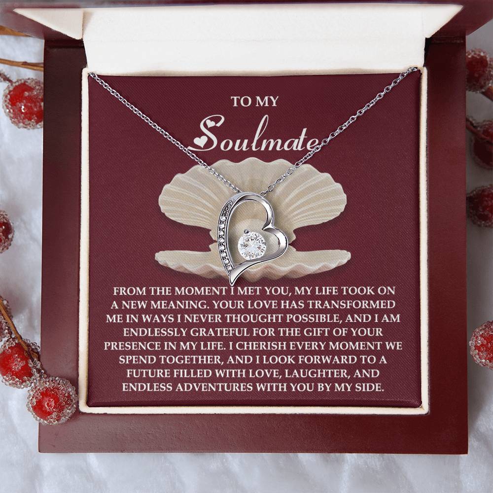 The Soulmate-Every Moment - Forever Love Necklace features a silver heart with a cubic zirconia gem, presented on a card with a heartfelt message, all nestled in an open box adorned with decorative red berries.