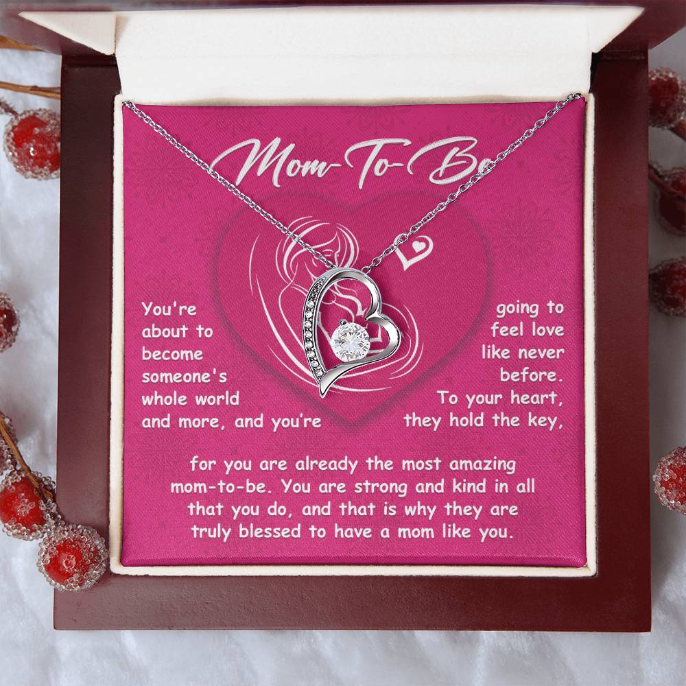 A jewelry box featuring the "To Mom To Be, Someone's Whole World - Forever Love Necklace." The background includes a heartfelt message for a mom-to-be on a pink card, making it one of the perfect personalized gifts.