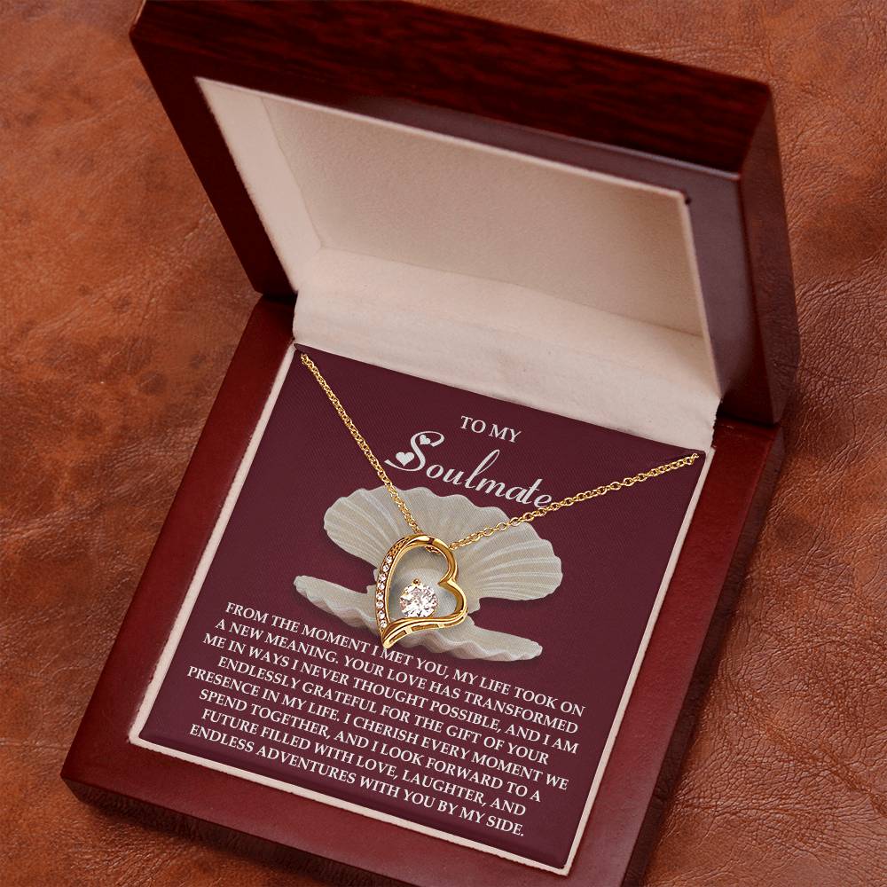 The Soulmate-Every Moment - Forever Love Necklace is a heart-shaped gold piece with a stunning cubic zirconia gemstone, presented in a wooden box. Inside the lid reads "To My Soulmate" with a heartfelt message, and the necklace rests on a rich brown surface symbolizing timeless affection.