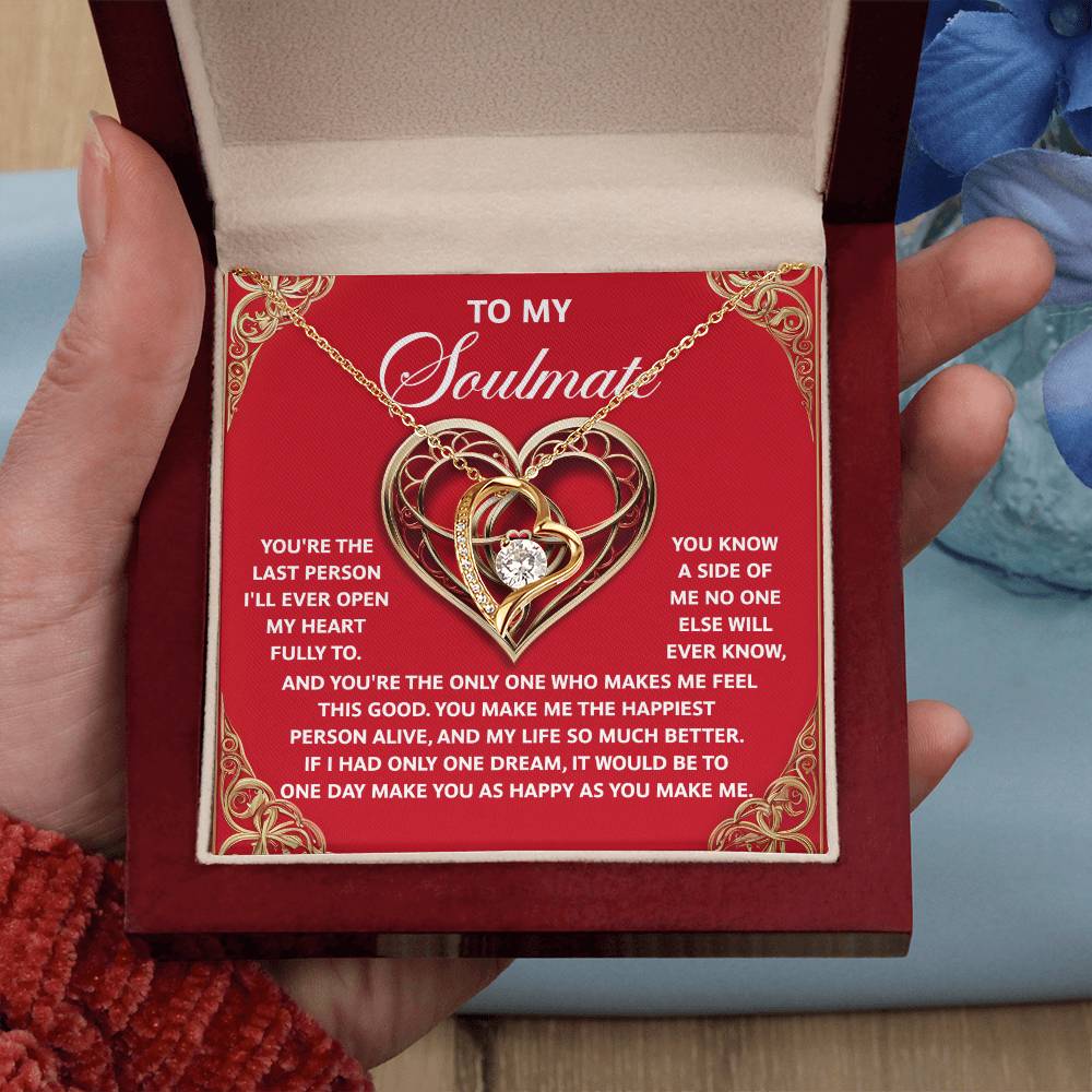 A person holds an open jewelry box containing the "Soulmate-The Only One - Forever Love Necklace." This gold-finish piece, featuring intertwined hearts and a central diamond, is ideal for your soulmate. The box lid displays a heartfelt poem expressing enduring love.