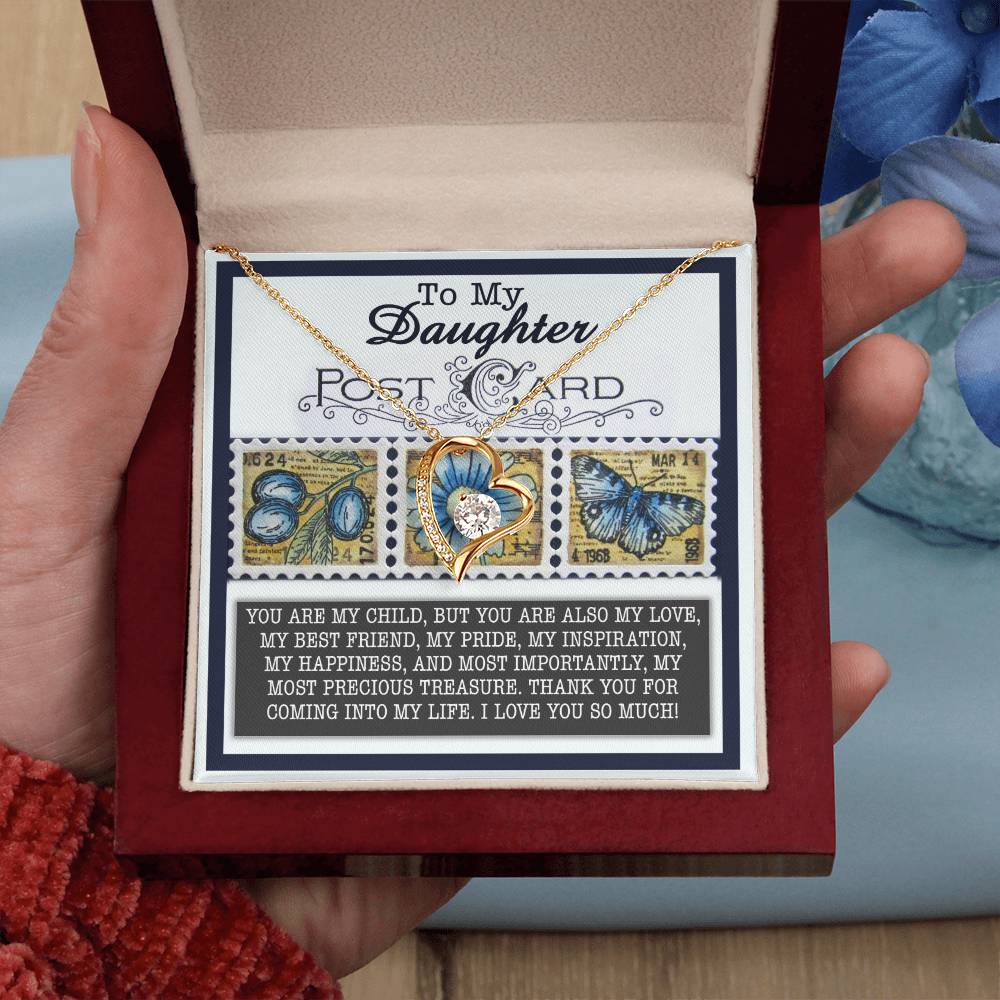 A heart-shaped "Daughter-Precious Treasure - Forever Love Necklace," featuring a butterfly design and adorned with CZ crystals in a white gold finish, rests elegantly in a gift box. It includes a heartfelt message and butterfly-themed stamps, making it the perfect expression of love.