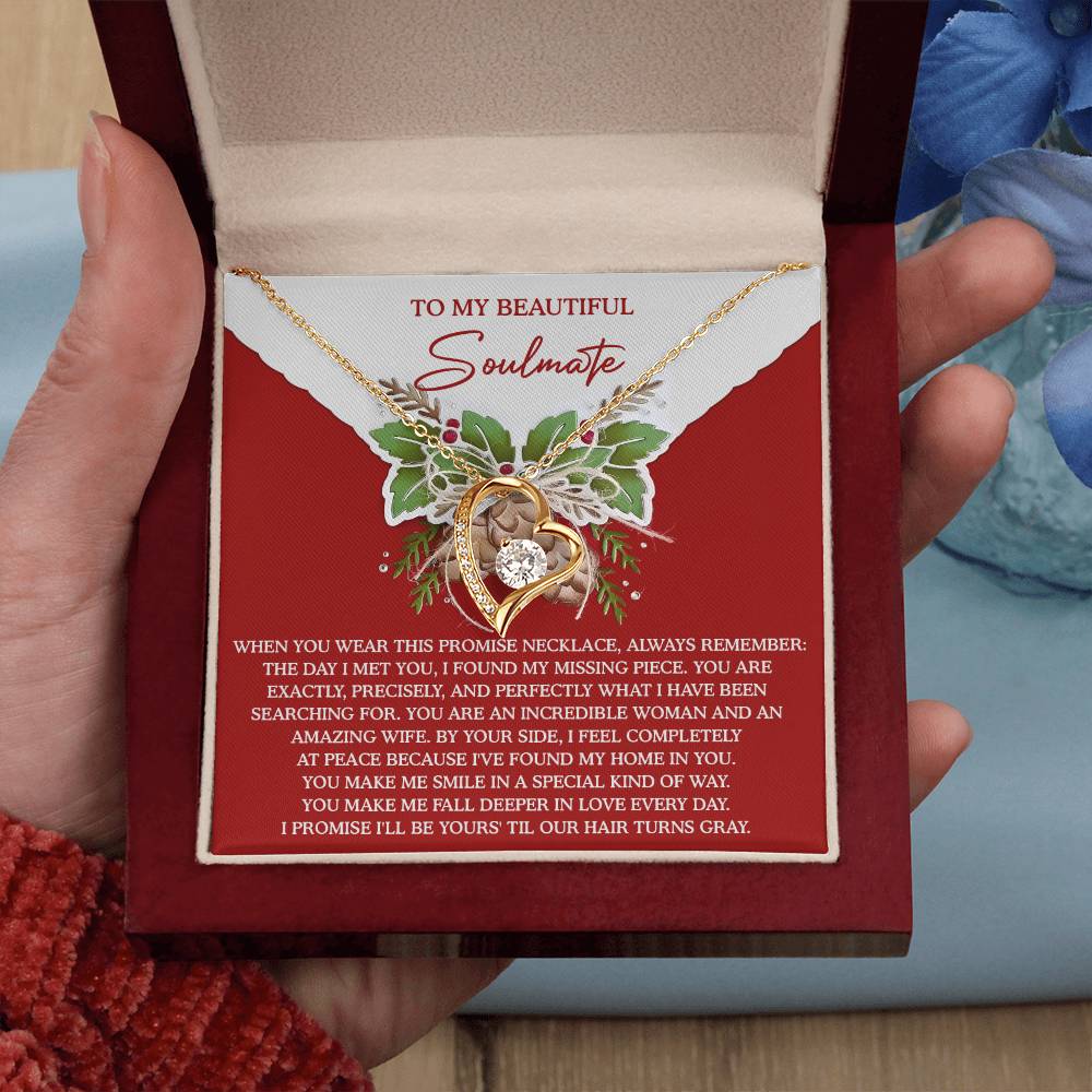 The Soulmate-At Peace - Forever Love Necklace showcases intertwined hearts embellished with cubic zirconia, all finished in elegant gold. It is presented in a box bearing the message, "To My Beautiful Soulmate," and is surrounded by graceful floral decor.
