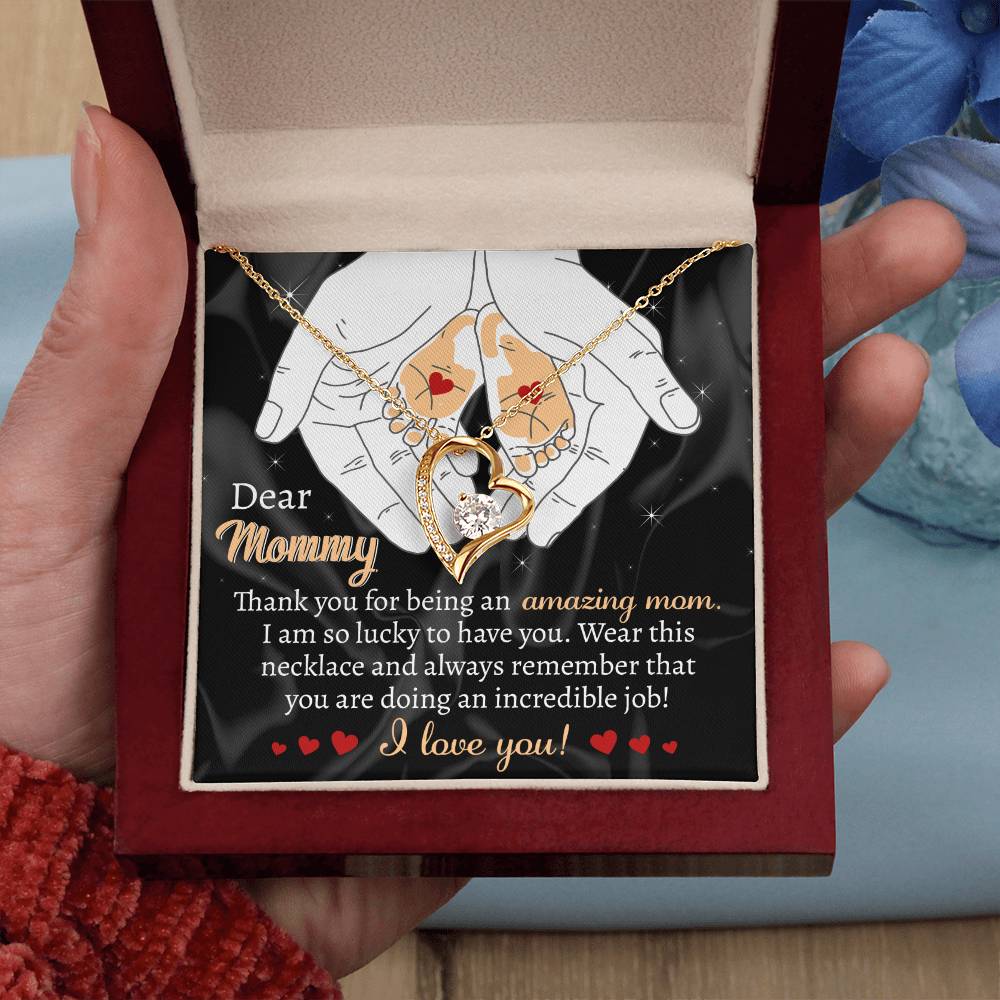 A hand holds an open jewelry box containing a heart-shaped white gold necklace. The box insert reads, "Dear Mommy, Thank you for being an amazing mom. I love you." This personalized gift exudes heartfelt sentiments, making it a perfect "To Mom To Be, An Incredible Job - Forever Love Necklace" for any cherished mother.