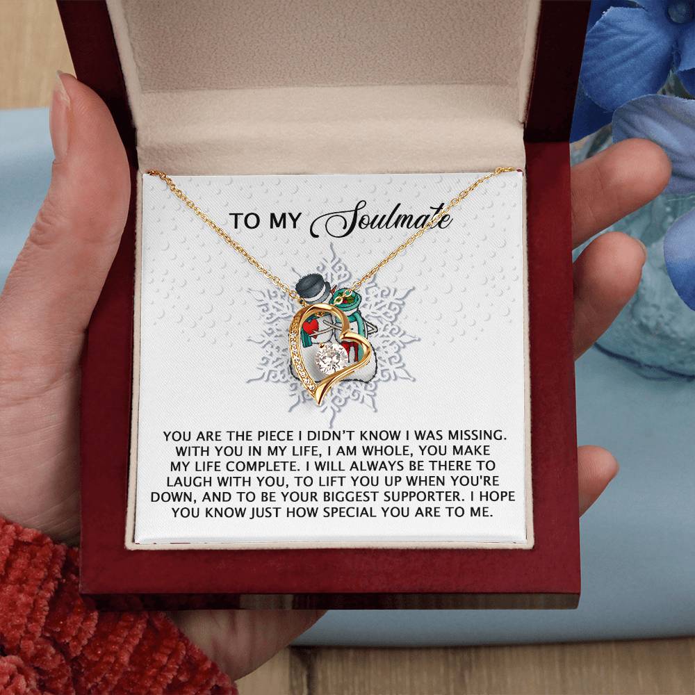 A hand presents an open jewelry box with the Soulmate-Laugh With You - Forever Love Necklace, showcasing a gold heart-shaped pendant adorned with rose designs and shimmering CZ crystals. A heartfelt message to a soulmate makes this the ideal gift.