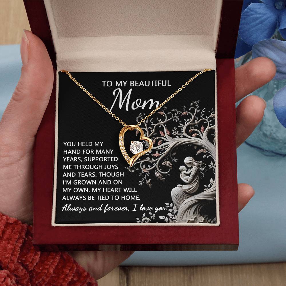 A hand holds an open red box containing the "To Mom, On My Own - Forever Love Necklace" with a heart-shaped gold pendant. The message inside, starting with "To My Beautiful Mom," expresses love and gratitude, making this personalized gift even more special.