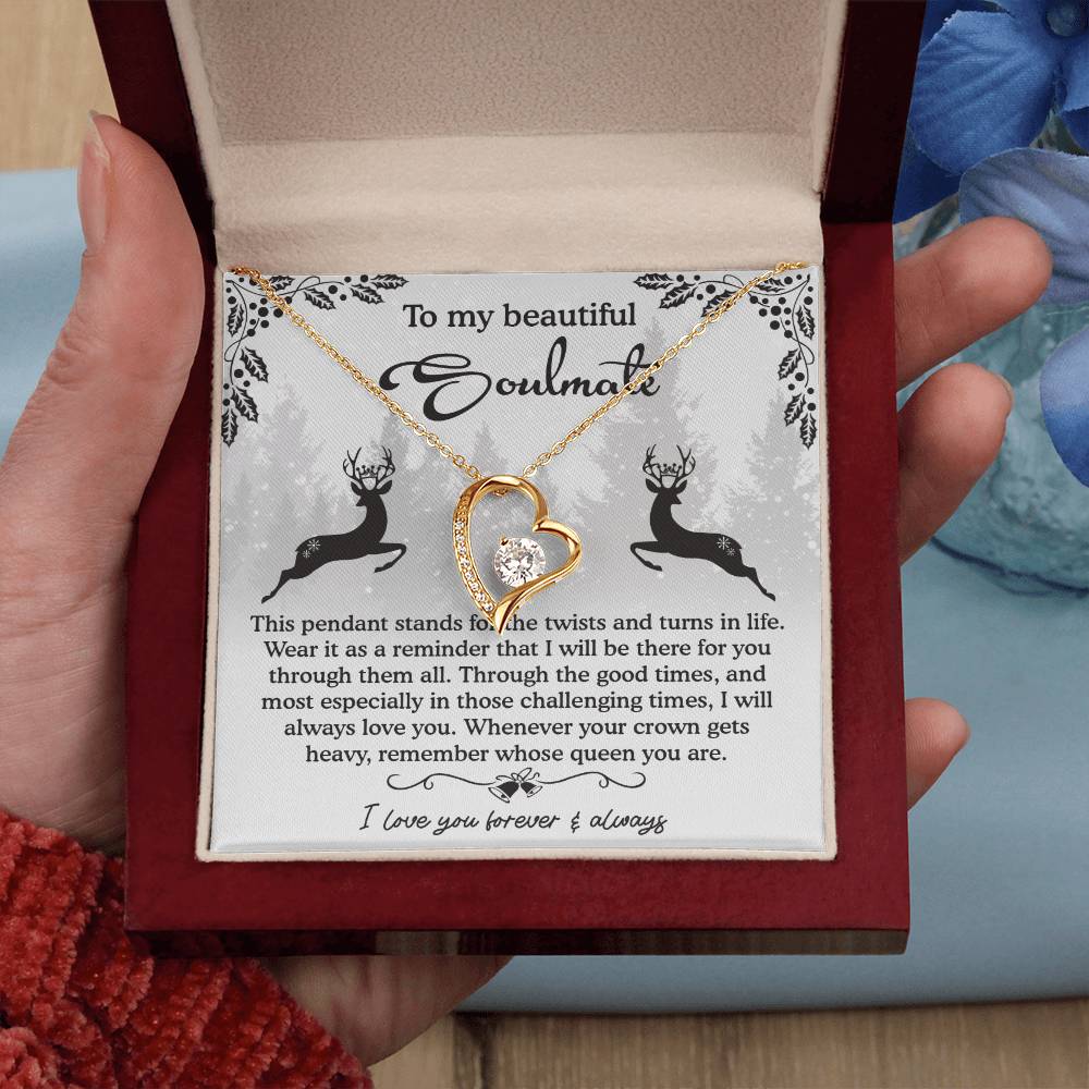 An open jewelry box displays a gold heart-shaped pendant—the Soulmate-A Reminder Forever Love Necklace with a gemstone. The background includes text and deer silhouettes, ideal for a personalized gift.
