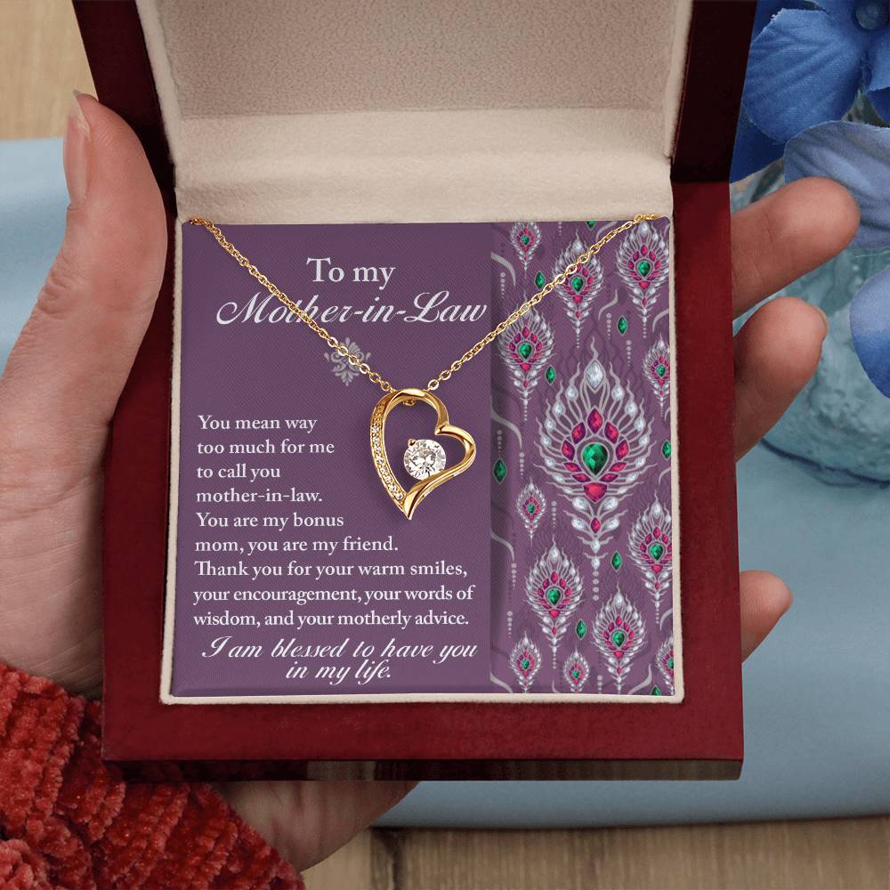 A hand holding an open jewelry box containing the "To Mother-In-Law, Words Of Wisdom - Forever Love Necklace" with a heart and crystal pendant. The box's interior has a heartfelt message to a mother-in-law along with a decorative pattern, making it the perfect personalized gift.