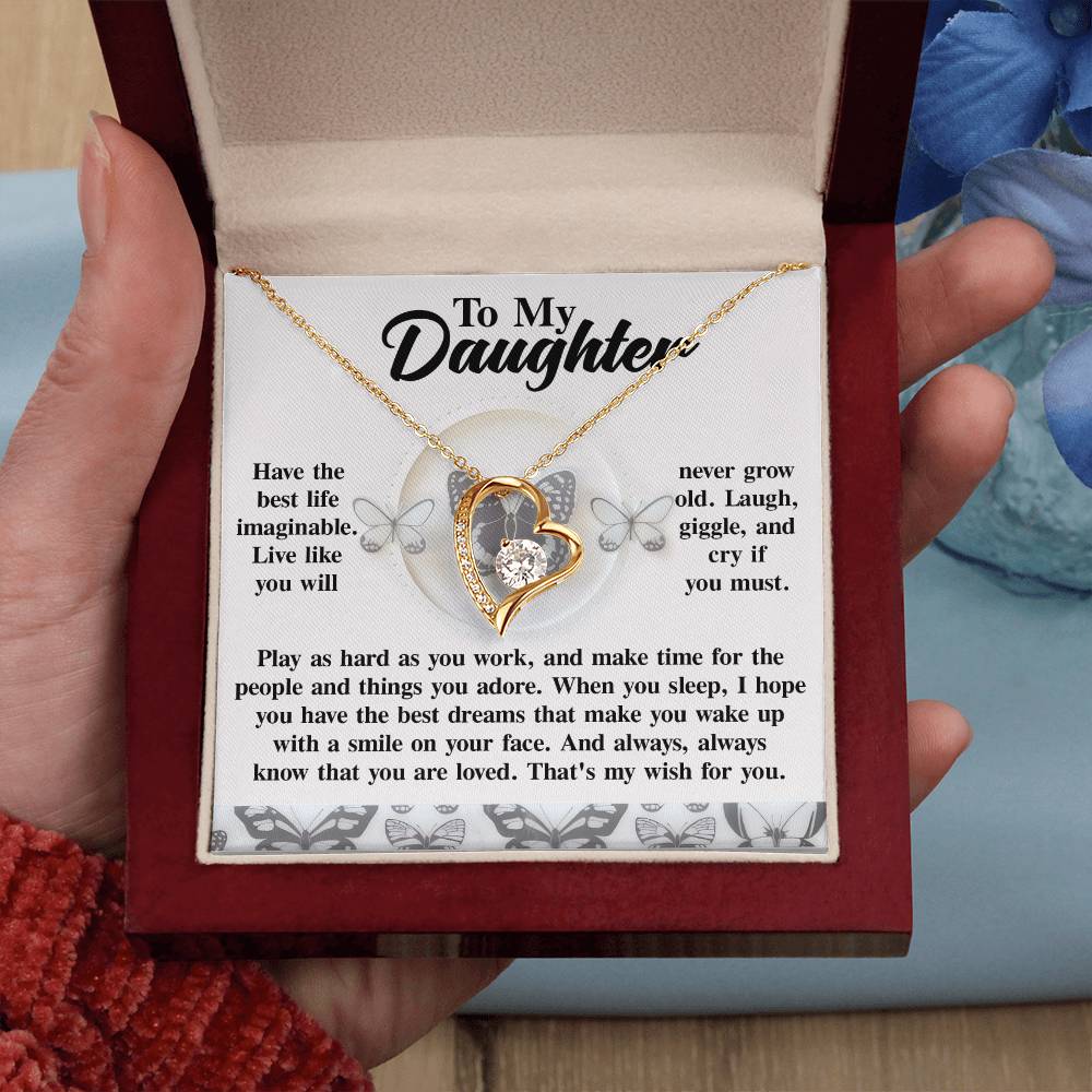 A hand presents an open jewelry box showcasing the Daughter-My Wish - Forever Love Necklace, featuring a gold heart pendant. The inside lid displays the message “To My Daughter,” and the necklace shines with a white gold finish, beautifully decorated with sparkling cubic zirconia.