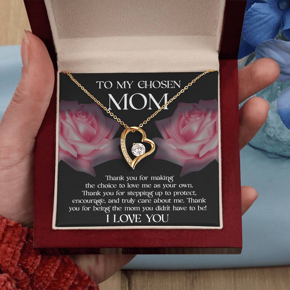 A hand holds an open jewelry box containing a To Bonus Mom, My Chosen Mom - Forever Love Necklace with a heart pendant in white gold finish. The interior reads a heartfelt note addressed to "Mom," expressing gratitude and love for choosing to be a mother, making it the perfect Mother's Day gift.