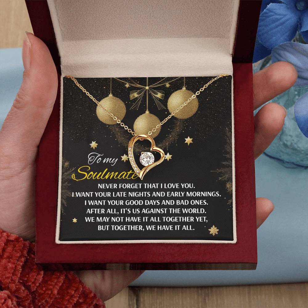 A hand presents an open jewelry box displaying the Soulmate-Have It All - Forever Love Necklace, which features a gold heart-shaped pendant adorned with a stunning CZ crystal. The necklace is accompanied by a card inscribed with a romantic message to a soulmate.