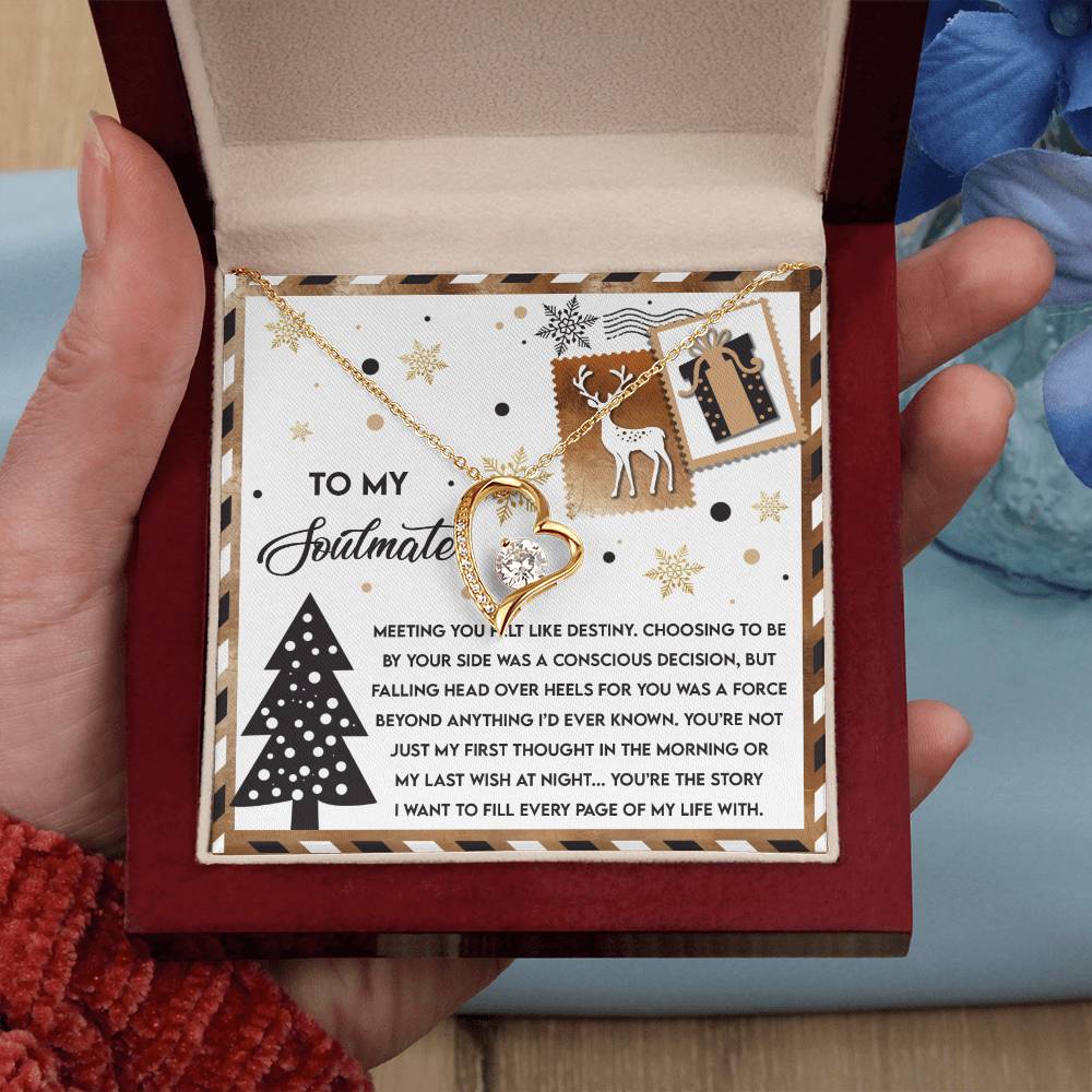 A hand opens a gift box, revealing the Soulmate-Like Destiny - Forever Love Necklace with its heart-shaped pendant elegantly displayed on a festive card adorned with text and holiday illustrations. This personalized gift embodies the spirit of celebrating with your soulmate.