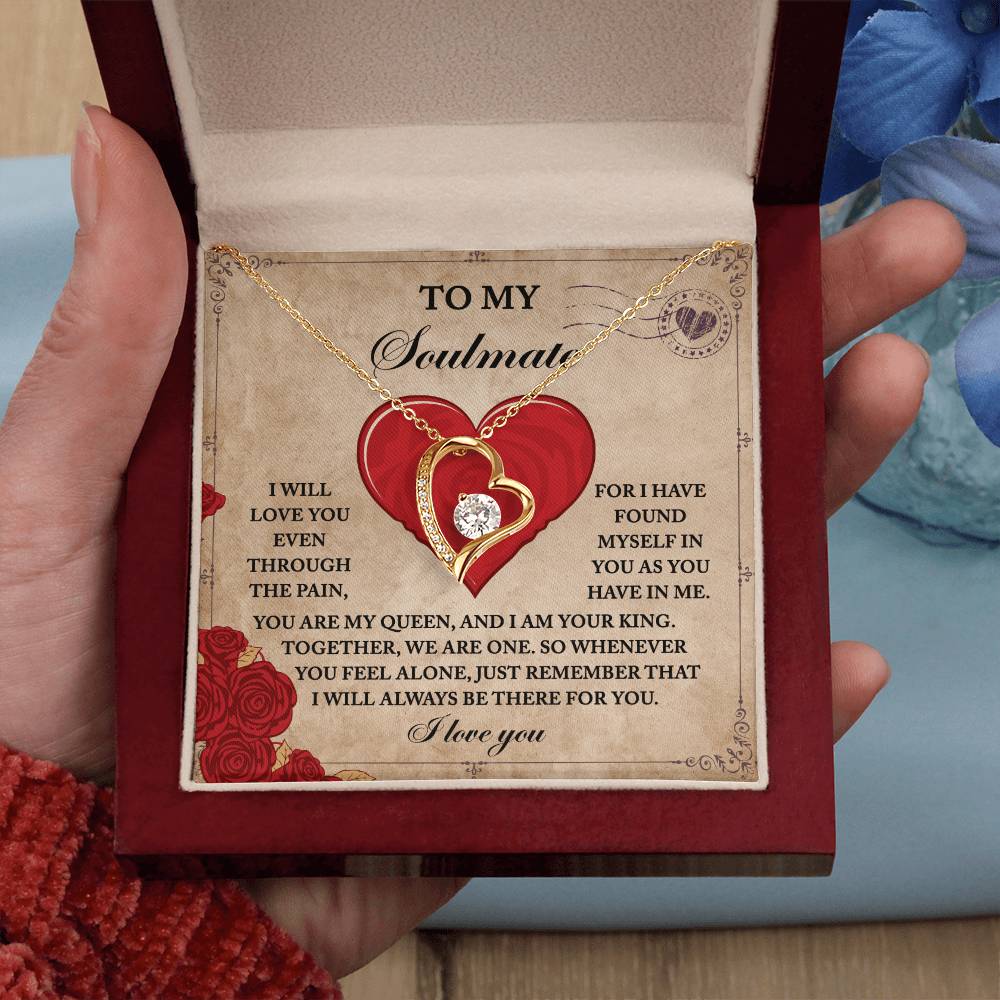 A person holds an open red jewelry box containing a Soulmate-Found Myself - Forever Love Necklace, featuring a heart-shaped pendant with a gold finish and sparkling cubic zirconia, accompanied by a heartfelt message to a soulmate.