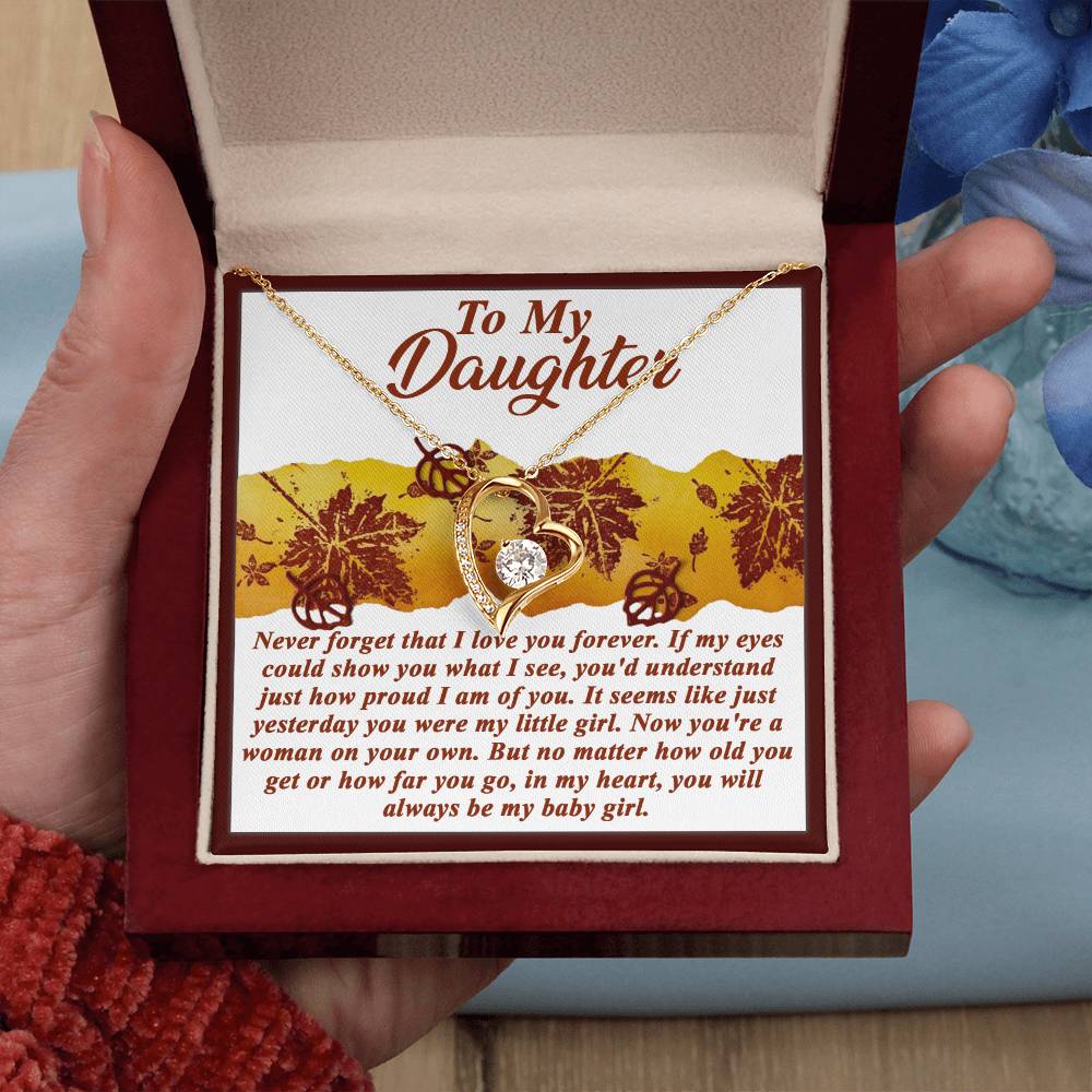 A hand holds an open box, unveiling a gold finish necklace adorned with a heart-shaped pendant. The *Daughter-On Your Own - Forever Love Necklace* beautifully features an engraved message dedicated to a daughter, embodying the sentiment of timeless love.