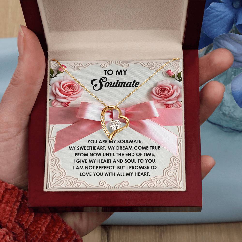 A hand opens a jewelry box to reveal the Soulmate-Heart And Soul - Forever Love Necklace with a CZ crystal heart pendant and gold finish, along with the message "To My Soulmate." The lid features a romantic note embellished with roses and a pink ribbon.