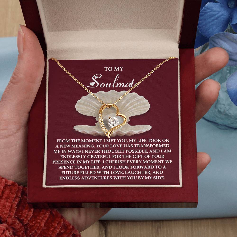A person holds the Soulmate-Every Moment - Forever Love Necklace box, showcasing a stunning gold heart-shaped pendant with cubic zirconia accents. An elegant inscription about love and gratitude graces the box, emphasizing its white gold finish.