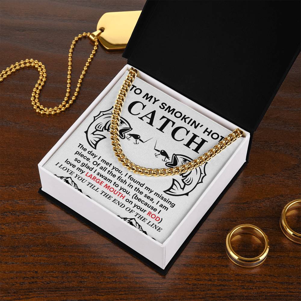 The Man-On Your Rod - Cuban Link Chain, a gleaming 14K yellow gold necklace, sits alongside a gold pendant and two polished stainless steel rings in an open box with a humorous fishing-themed message on a wooden surface.