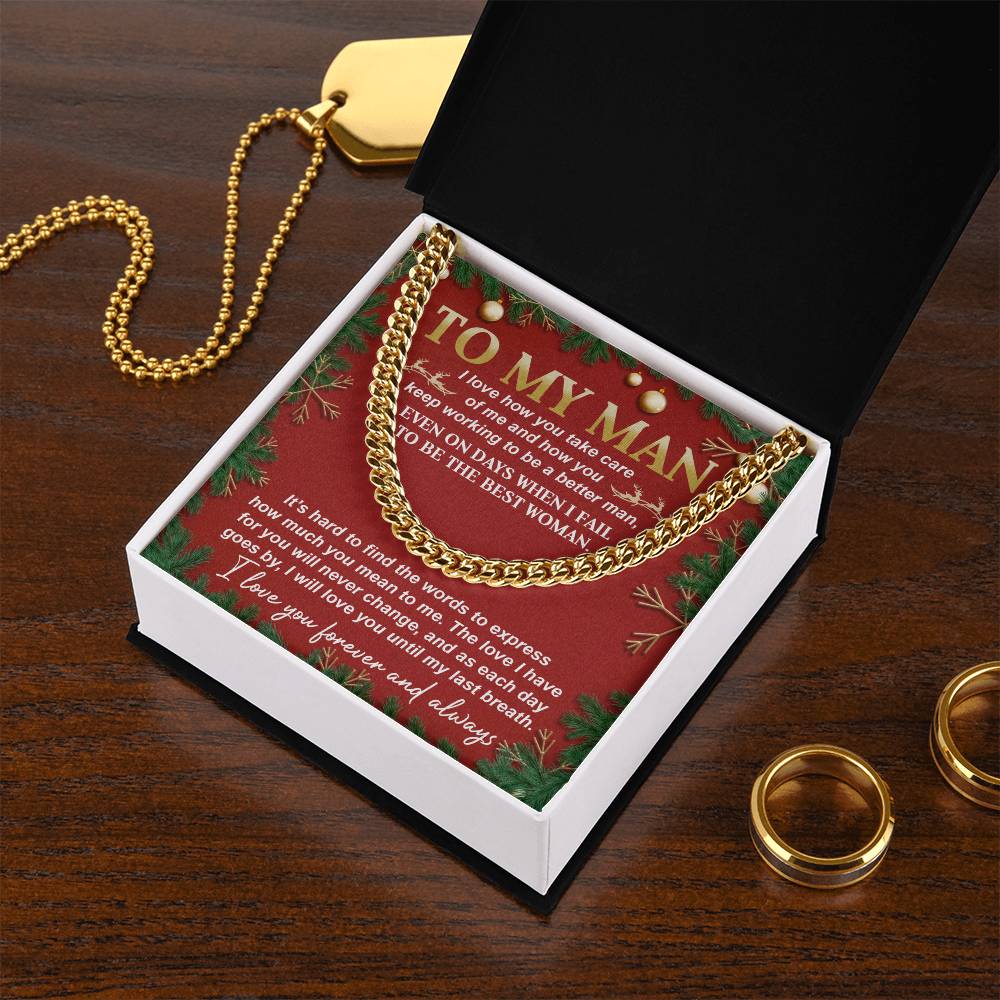 A My Man-Never Change - Cuban Link Chain glimmers in an open black box, accompanied by a card that reads, "To My Man," against a red holiday-themed backdrop. Nearby, two gold rings and a classic necklace gracefully rest on a wooden surface.
