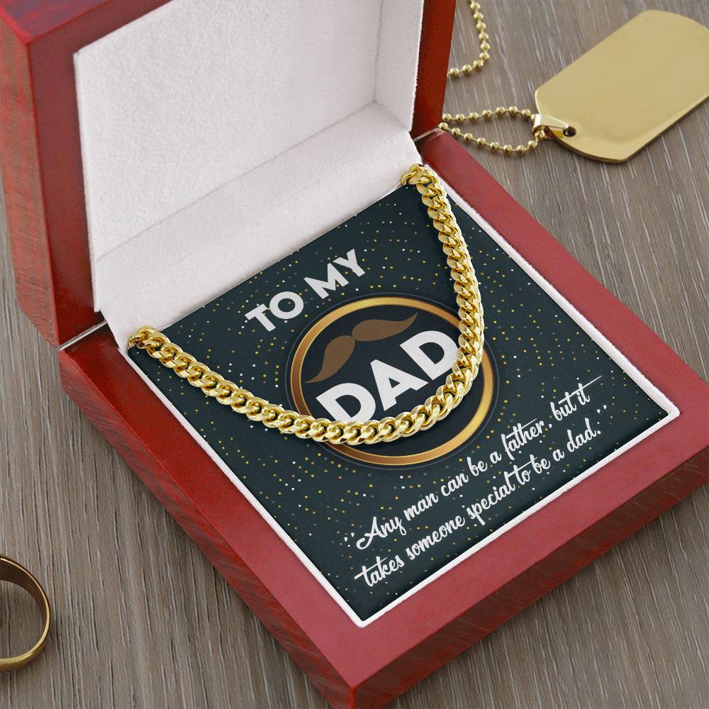The "To Dad, Be A Dad - Cuban Link Chain" necklace sits elegantly in a red box with a card saying "To My Dad" and a heartfelt message. An adjustable length ensures a perfect fit, complemented by a gold tag and ring on the wooden surface.