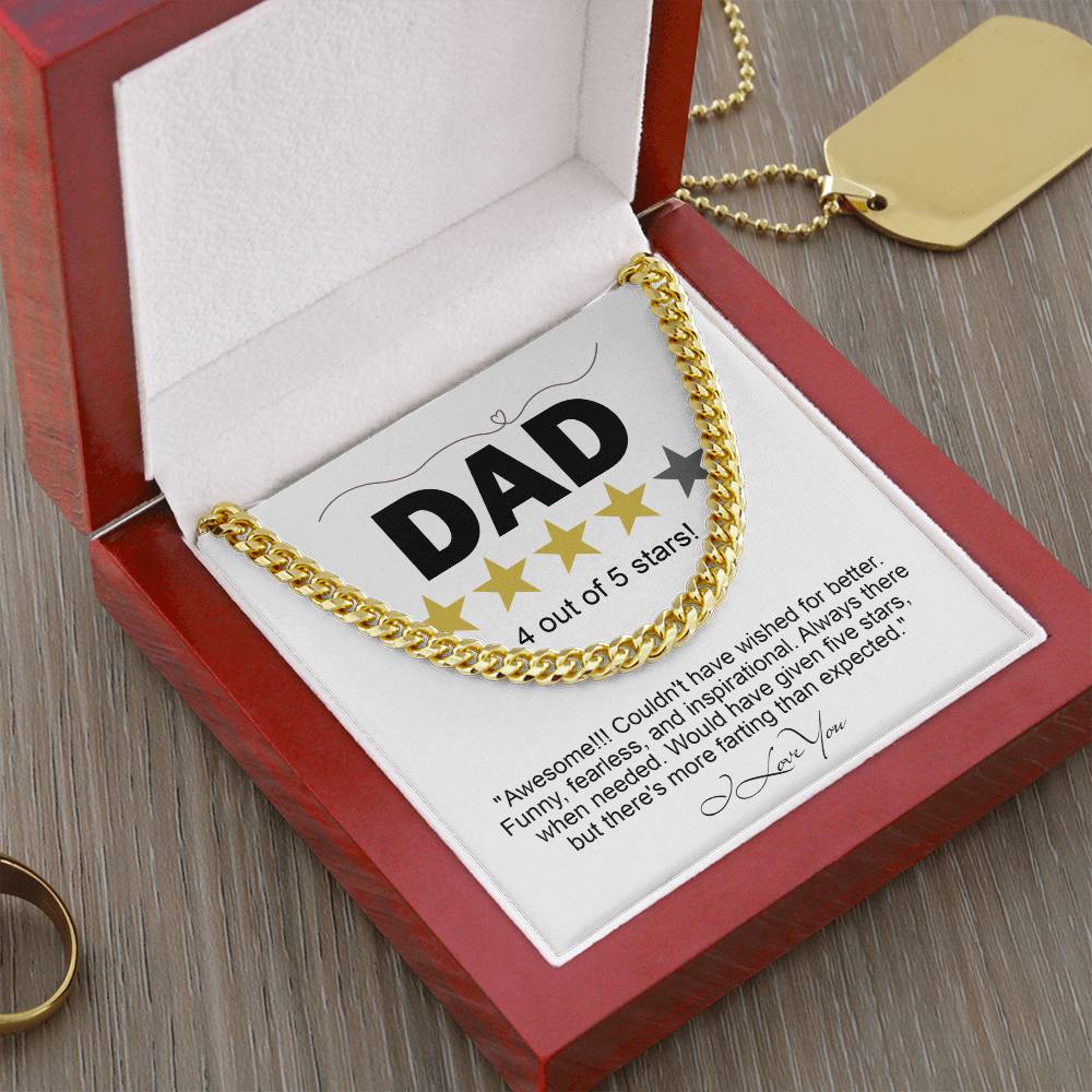 A "To Dad, Five Stars - Cuban Link Chain" in 14K yellow gold is elegantly showcased in an open wooden box. Inside, a card reads "DAD" with a 4-star rating, accompanied by a humorous review and signature. This sophisticated necklace enhances any occasion.