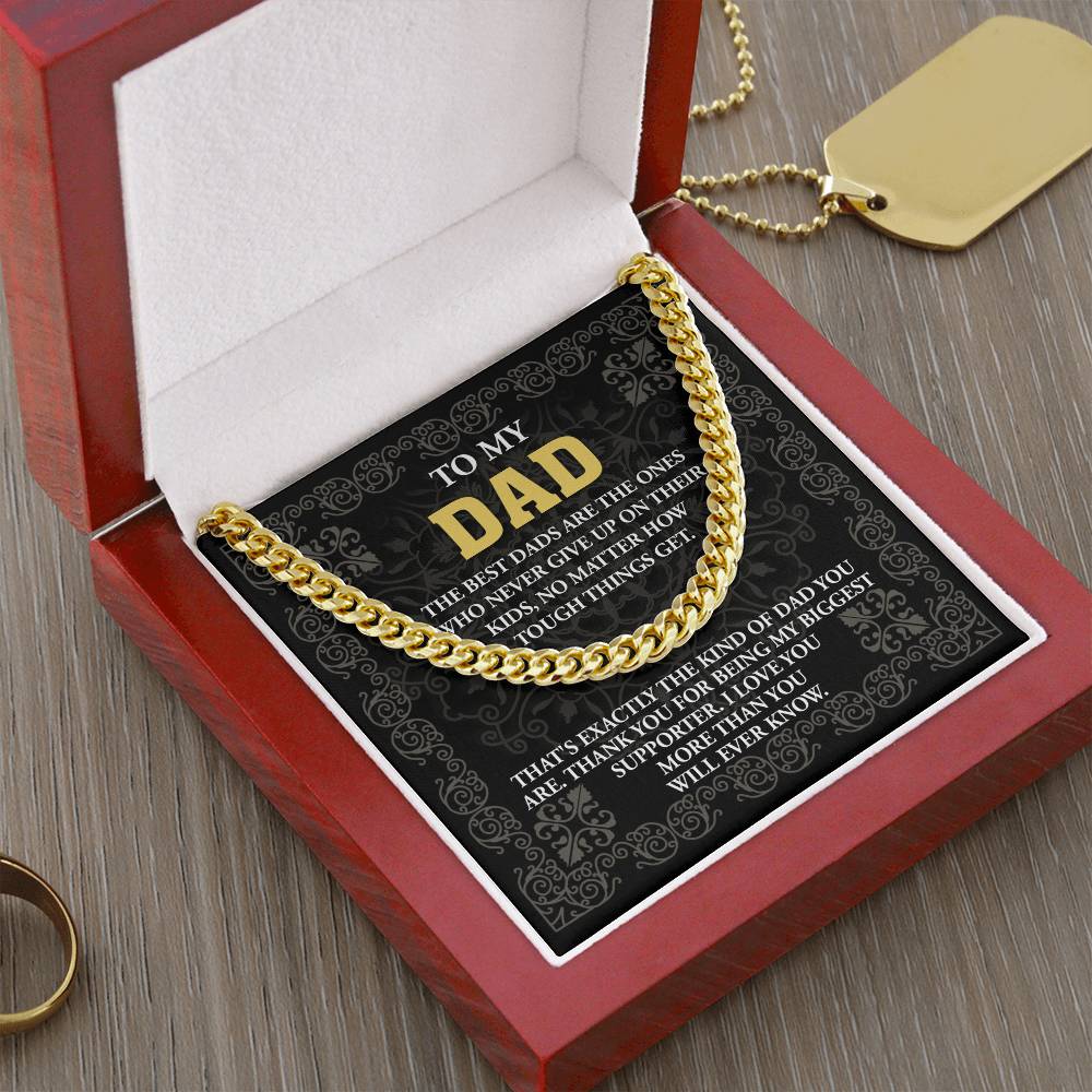 The "To Dad, Kind Of Dad - Cuban Link Chain" is a personalized gift featuring a gold chain in a red velvet box and includes a heartfelt message card for dad. The adjustable necklace delicately shines on a wooden surface.