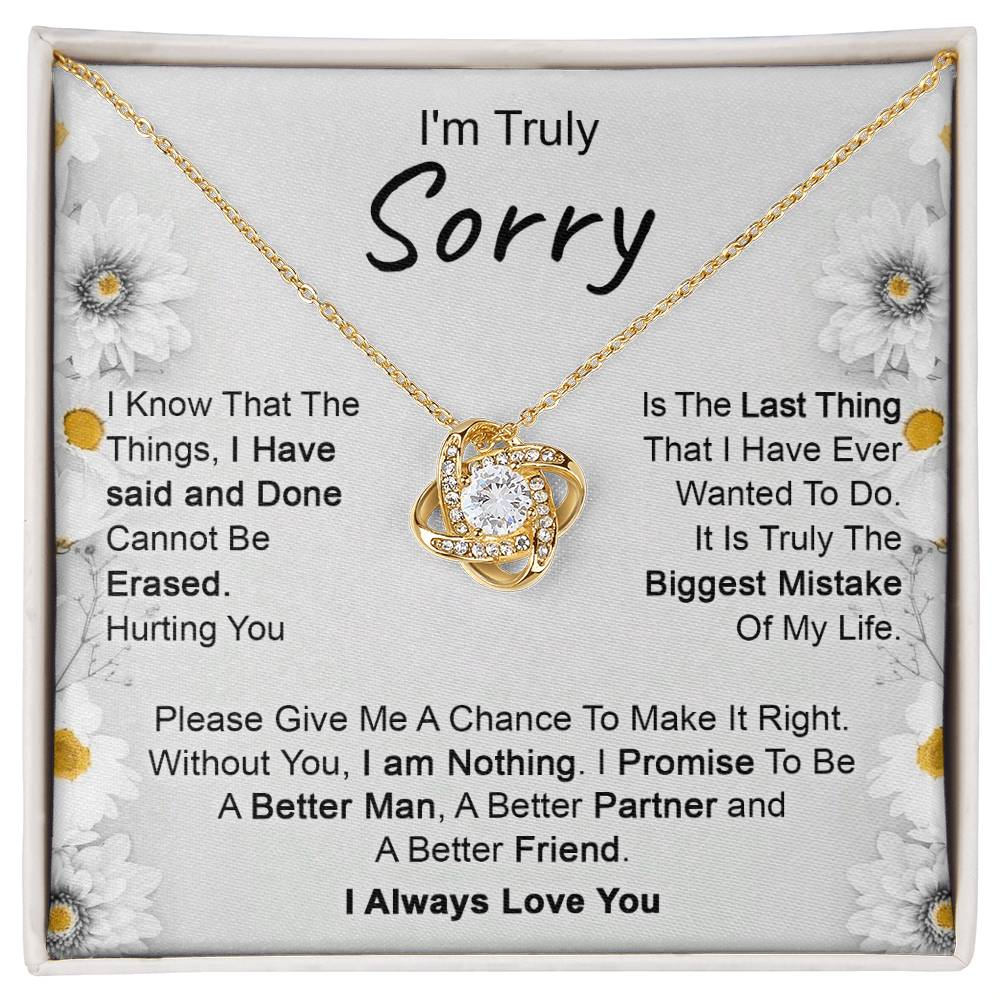 The "I’m Truly Sorry - Love Knot Necklace," featuring a pendant adorned with cubic zirconia crystals, rests on a heartfelt message that reads, "I'm Truly Sorry." The text conveys remorse for past actions and a commitment to becoming a better person, partner, and friend. The background is decorated with delicate floral designs.