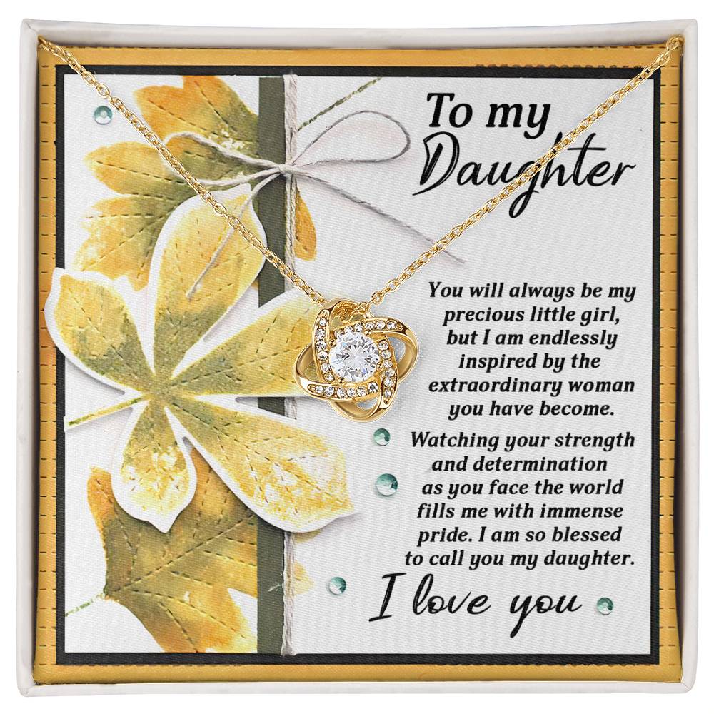 The Daughter-Blessed To Call - Love Knot Necklace, featuring a yellow gold finish and cubic zirconia crystals, is showcased on a card with a heartfelt message to a daughter expressing pride, inspiration, and love. The display includes a background with a leafy design.