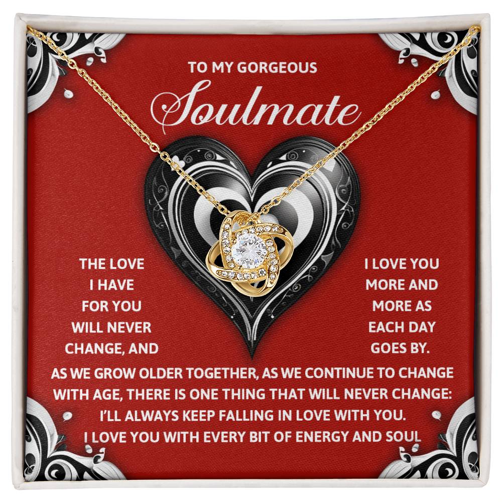 The Soulmate-Energy And Soul - Love Knot Necklace showcases a heart-shaped pendant with cubic zirconia crystals on a red background. Its black and silver design, paired with heartfelt text, beautifully embodies enduring love, making it an ideal personalized gift for your soulmate.