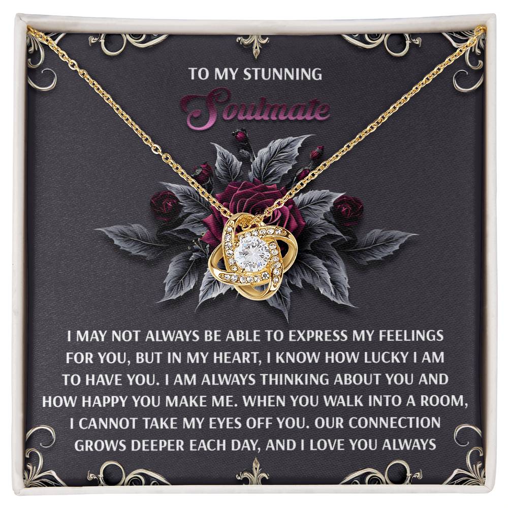 The Soulmate-Eyes Off You Love Knot Necklace features a large central gem on a dark floral background, with text expressing love for a soulmate. It’s beautifully set in timeless white gold, perfect for symbolizing an unbreakable bond.
