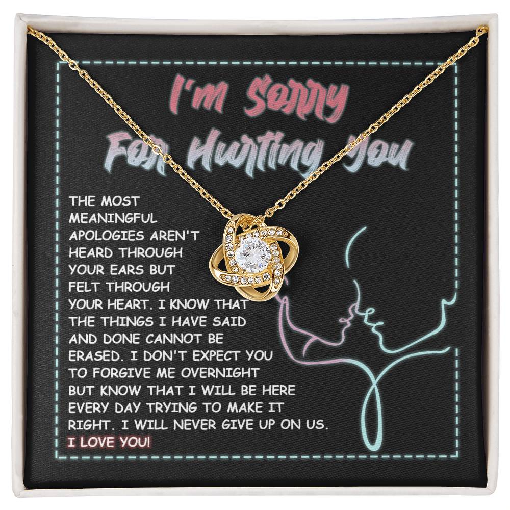 A 14k white gold Sorry-Never Give Up - Love Knot Necklace with an interlocked pendant set with cubic zirconia crystals sits on a note that reads, "I'm sorry for hurting you," accompanied by an apology message expressing regret, commitment to make things right, and affirming love.